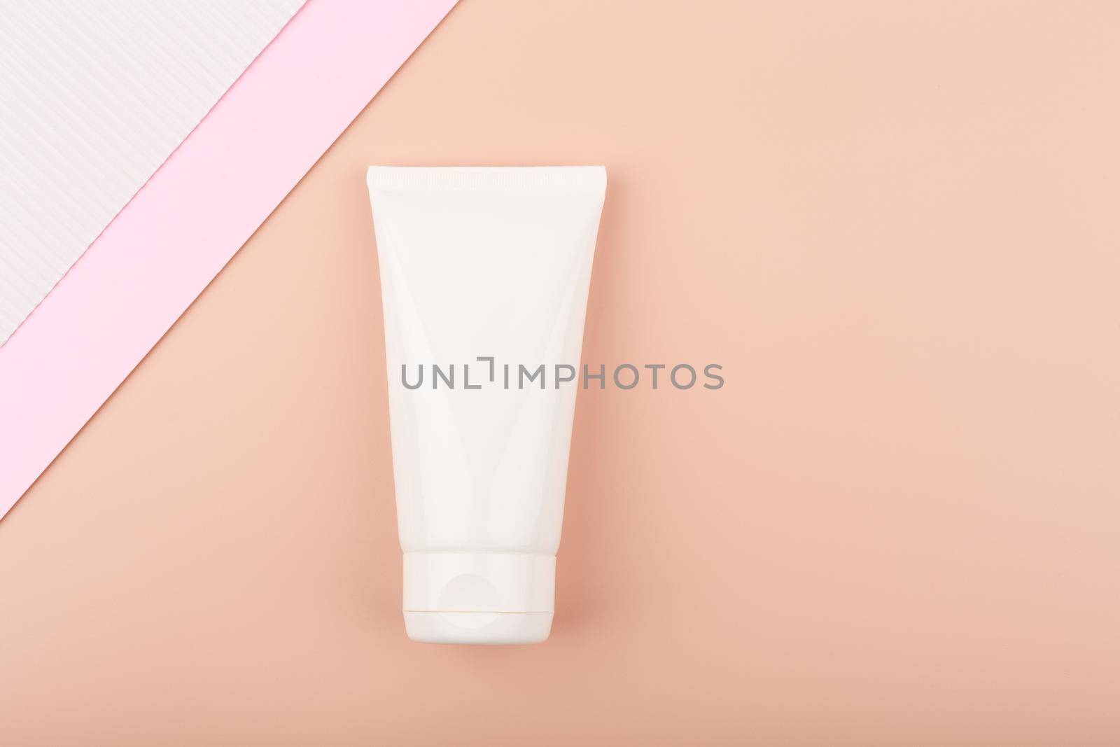 White cream tube with face or hand cream on pastel pink background decorated with white and pink paper by Senorina_Irina