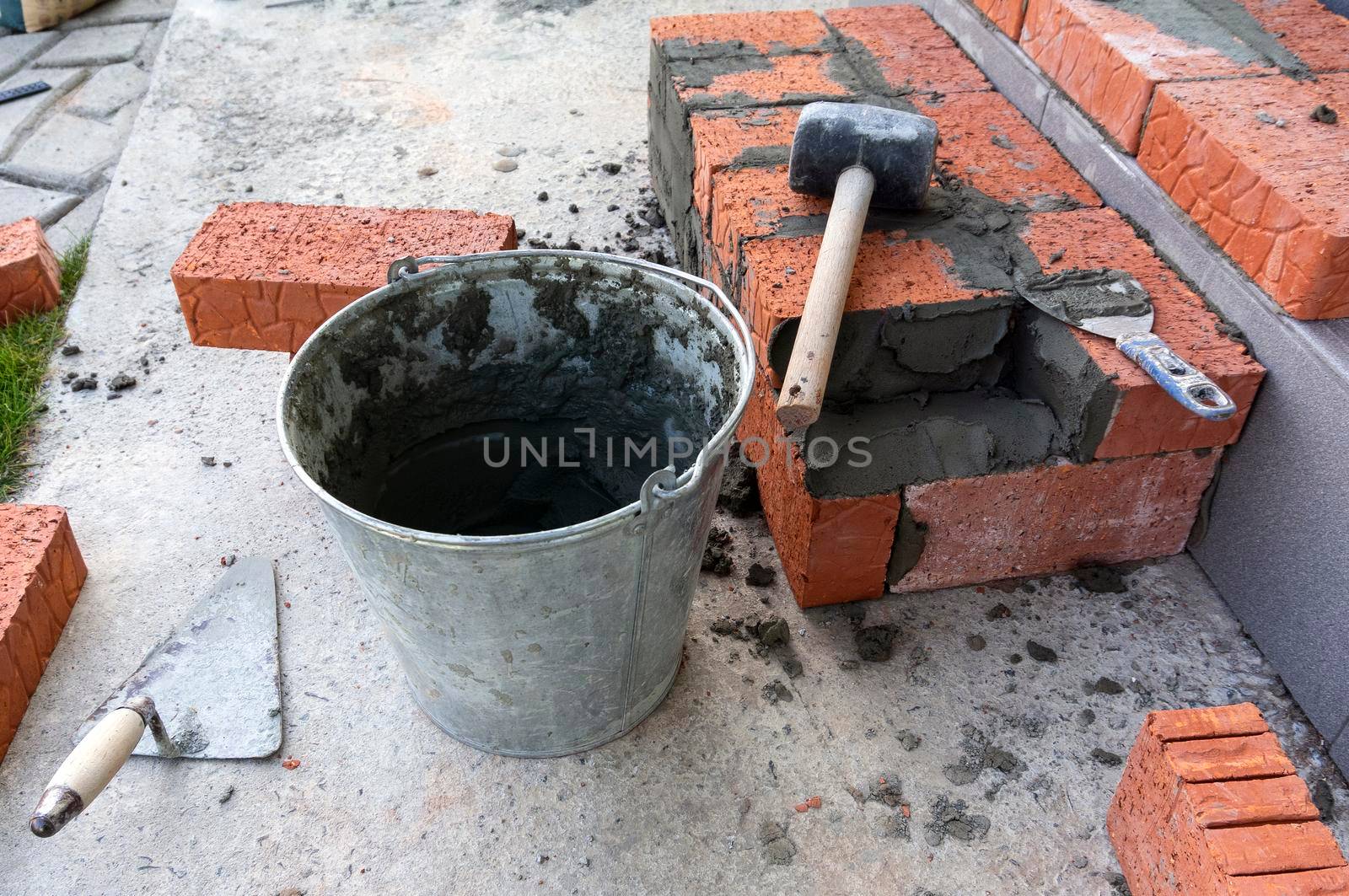 Bucket with a solute, trowel, rubber mallet and clay bricks