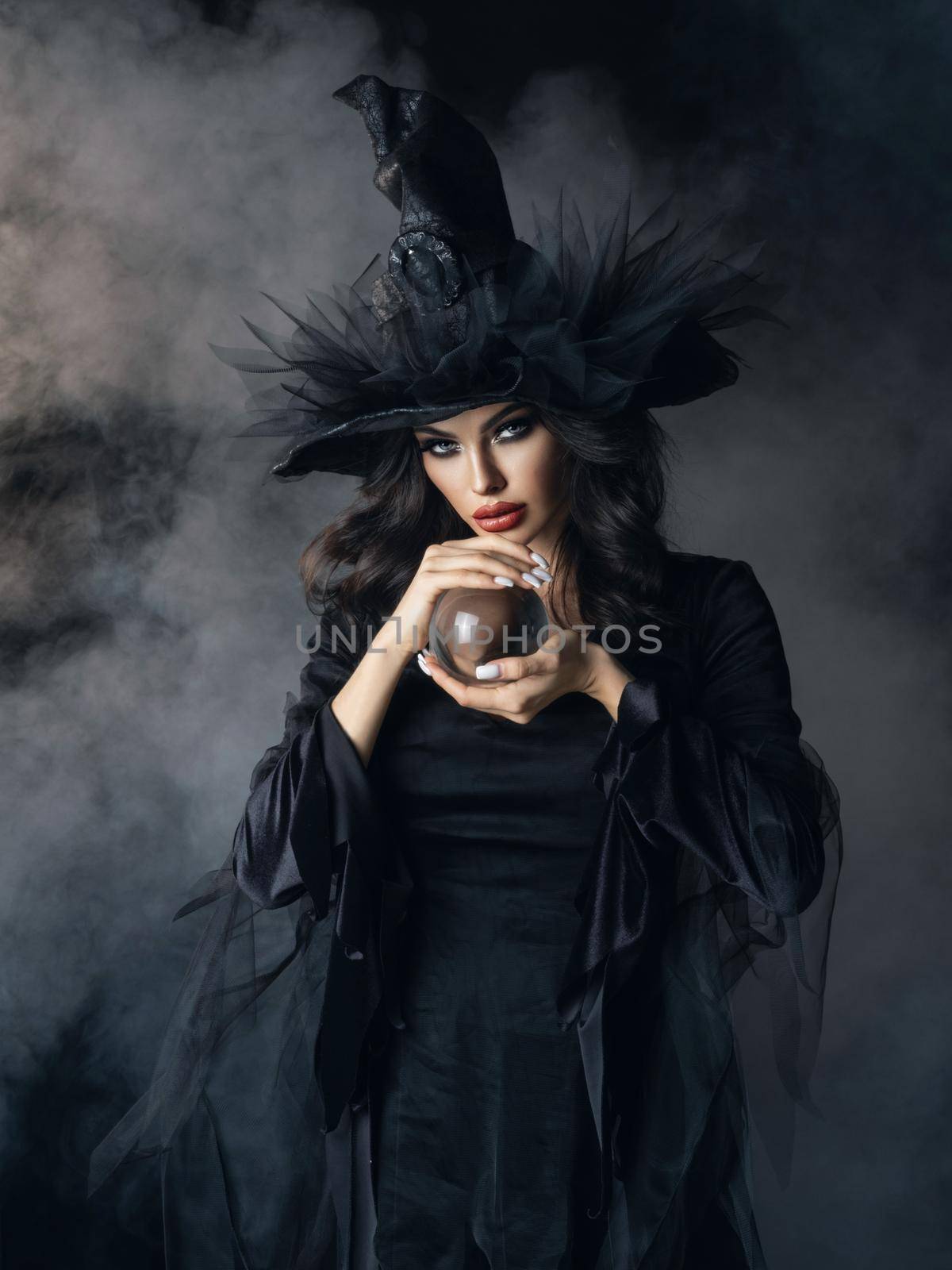Woman in Halloween witch costume with crystal ball. Beautiful sexy model girl in sinister costume and make up