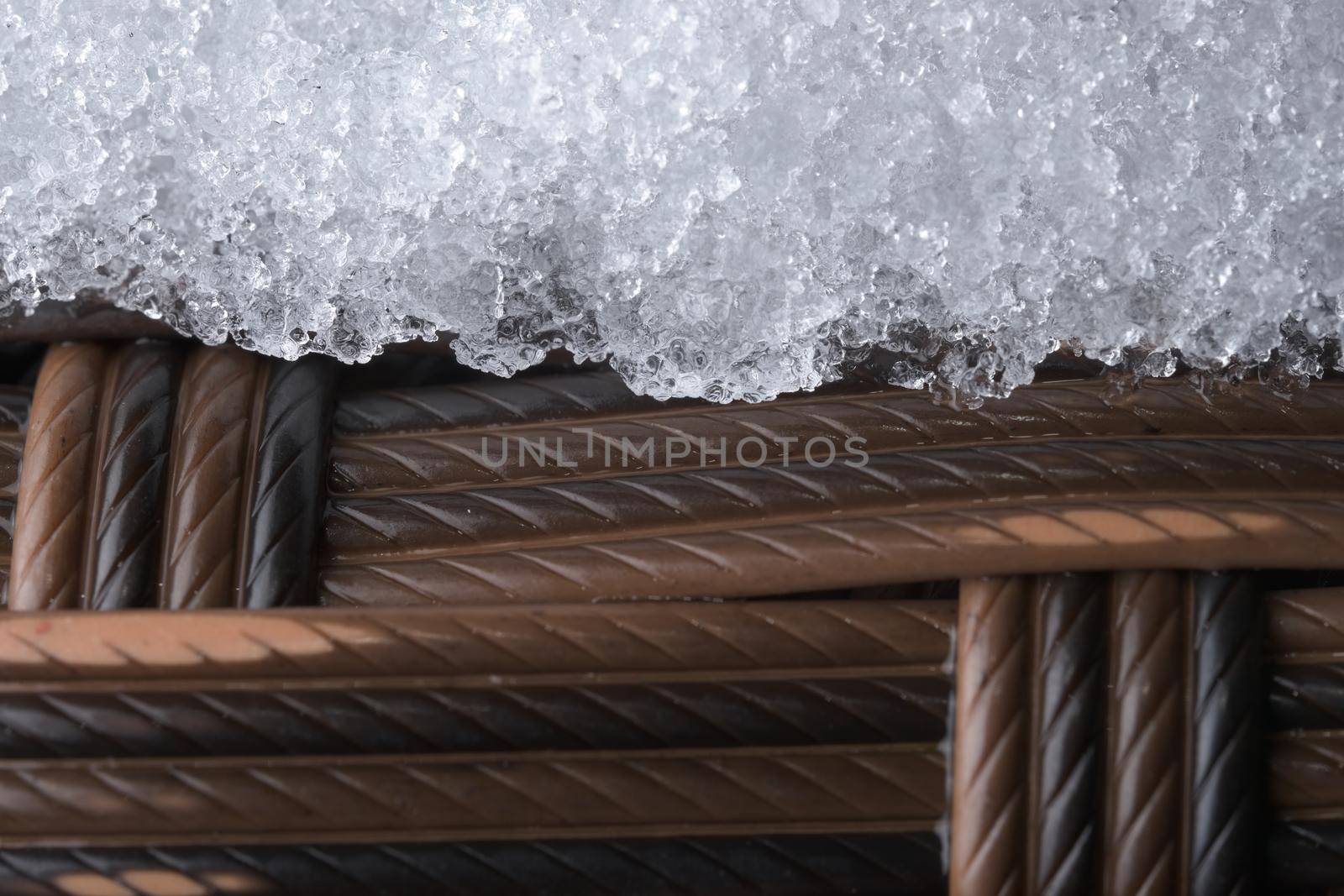Icy plastic garden furniture. Rattan style weave, but synthetic material. Cold outdoor weather has caused a layer of snow or frost to settle.