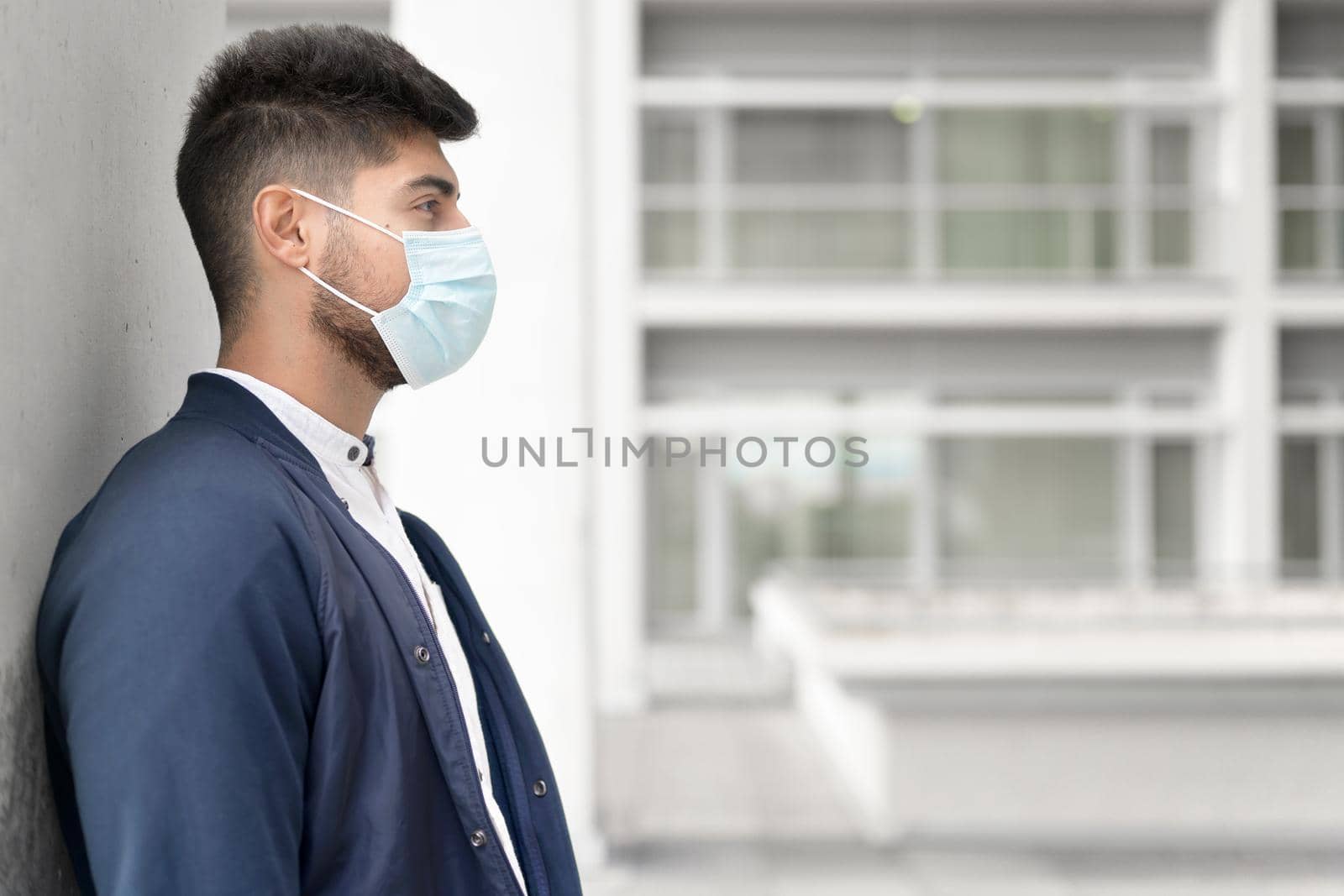 Handsome young man standing outdoors in medical mask. Coronavirus concept. by HERRAEZ