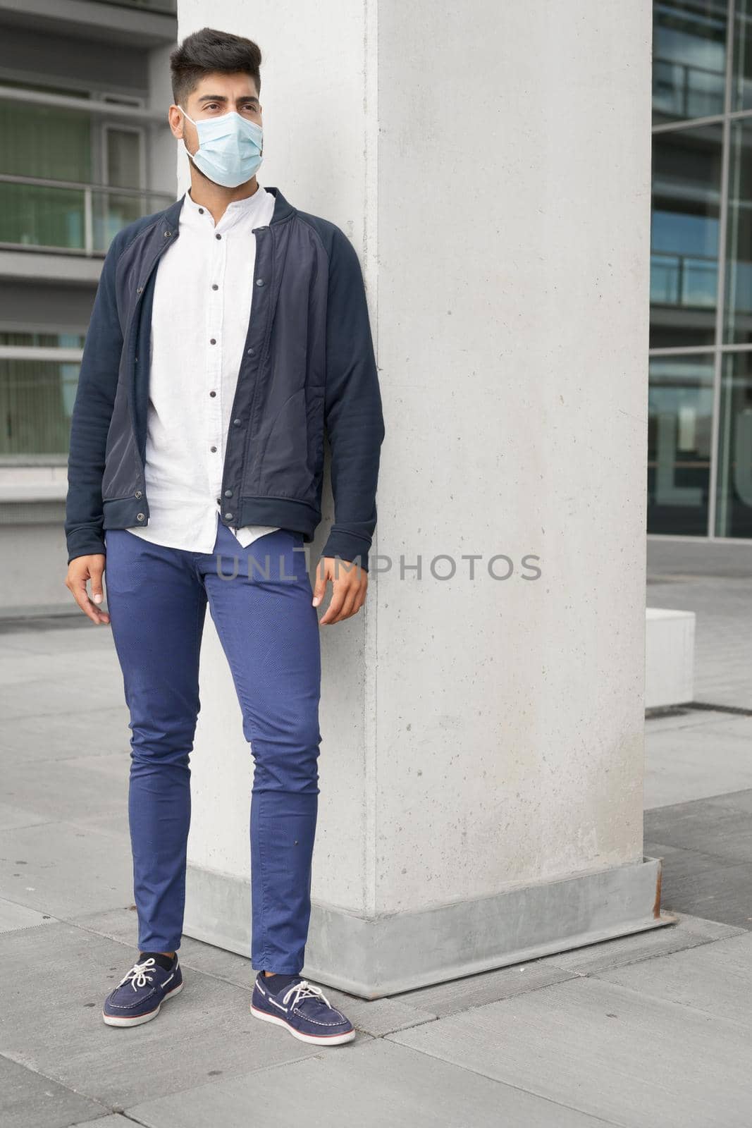 Handsome young man standing outdoors in medical mask. Coronavirus concept. by HERRAEZ