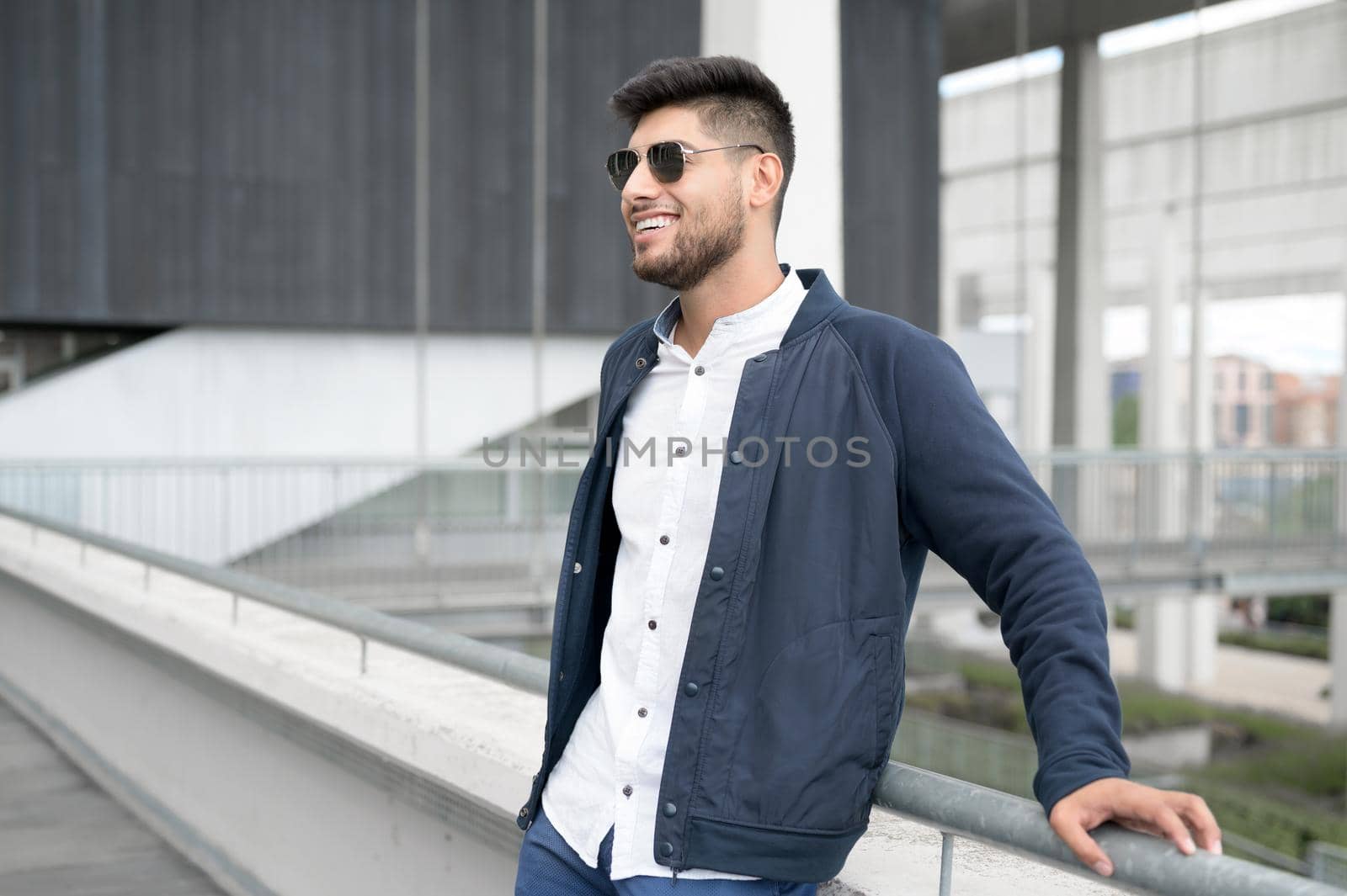 Portrait of a young confident smiling man standing beside modern building looking into the distance. High quality photo