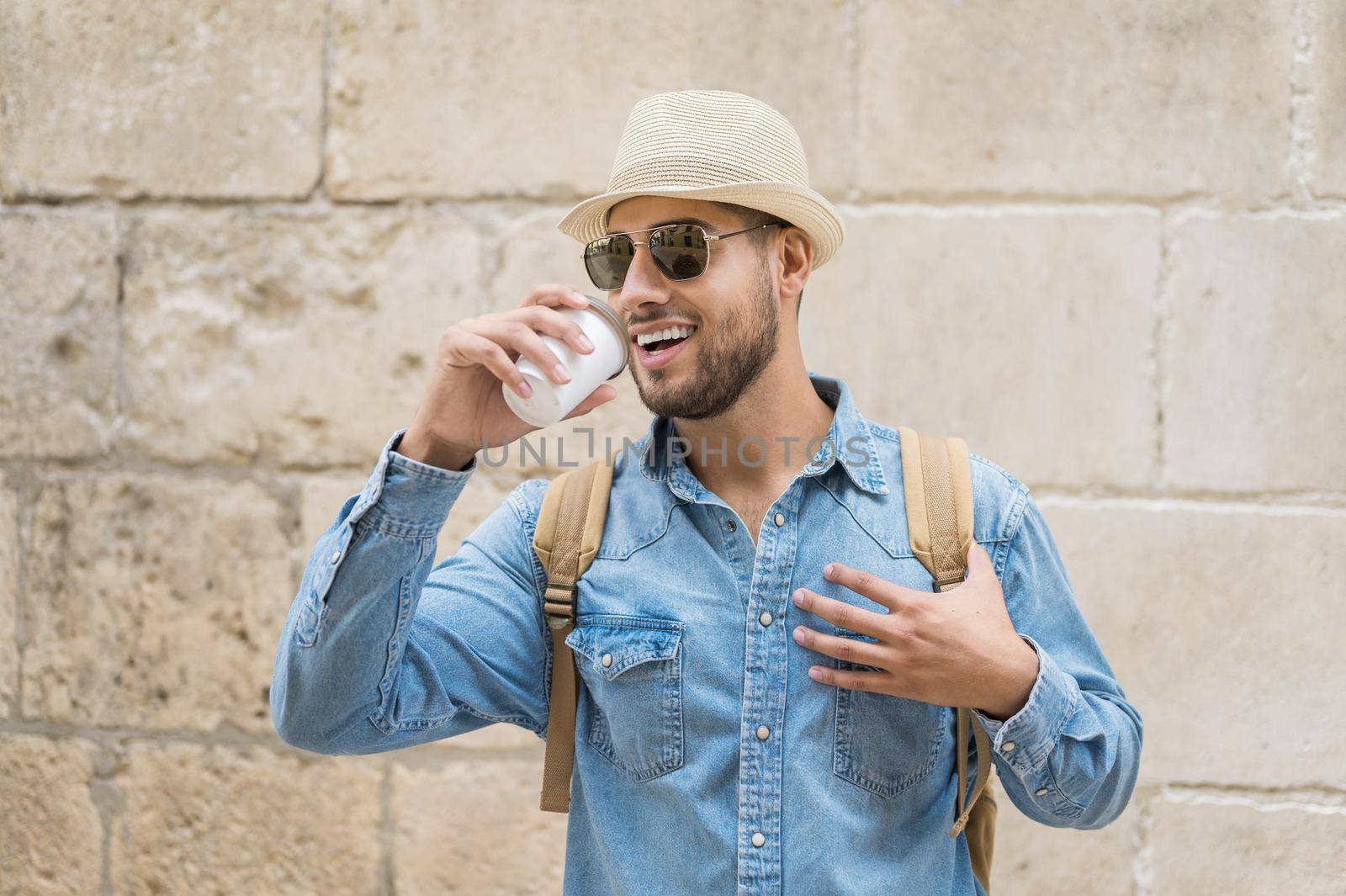 Happy young tourist man with coffee to go and backpack walking on street. High quality photo