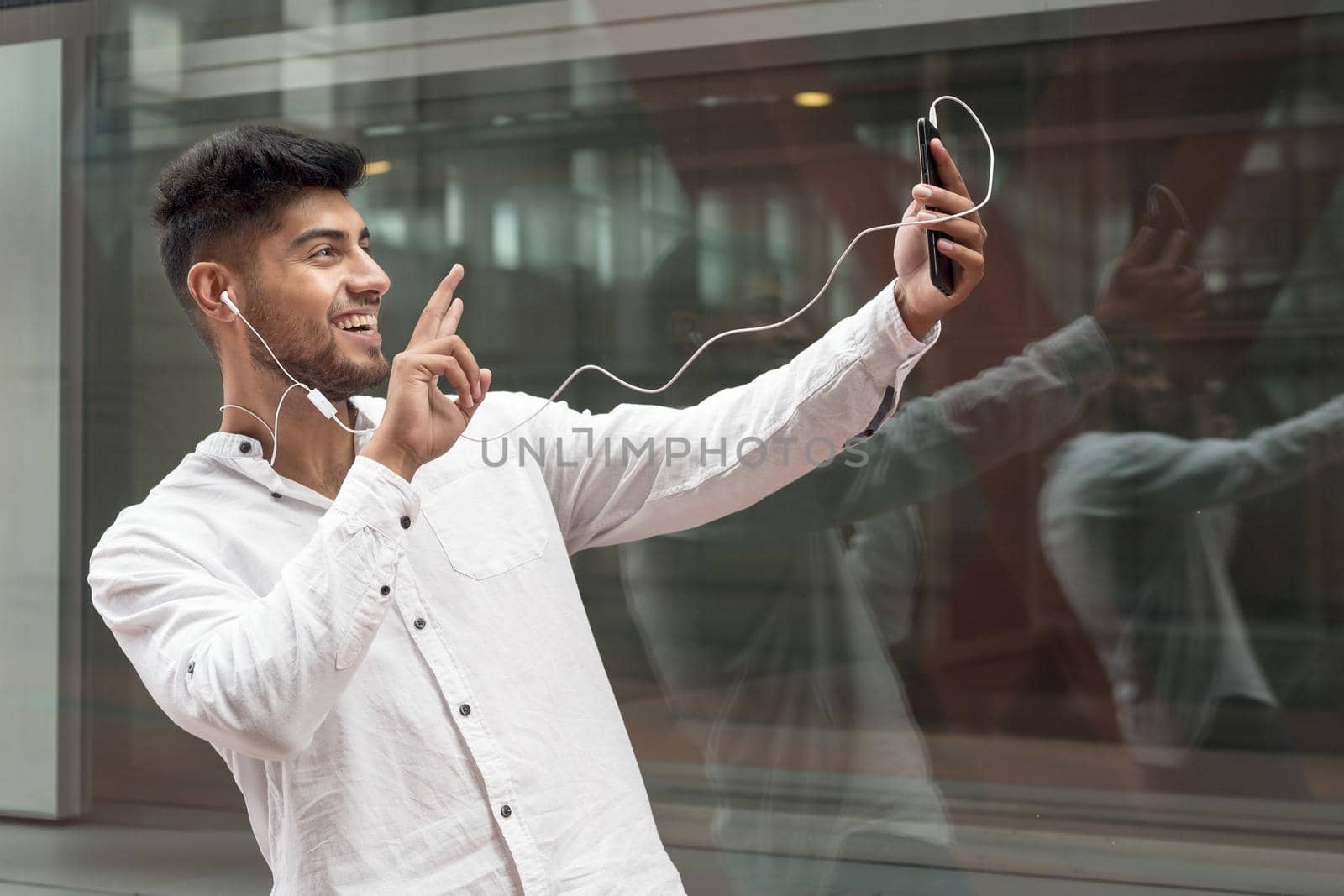 Young man smiling happy doing video call using smartphone at city. by HERRAEZ