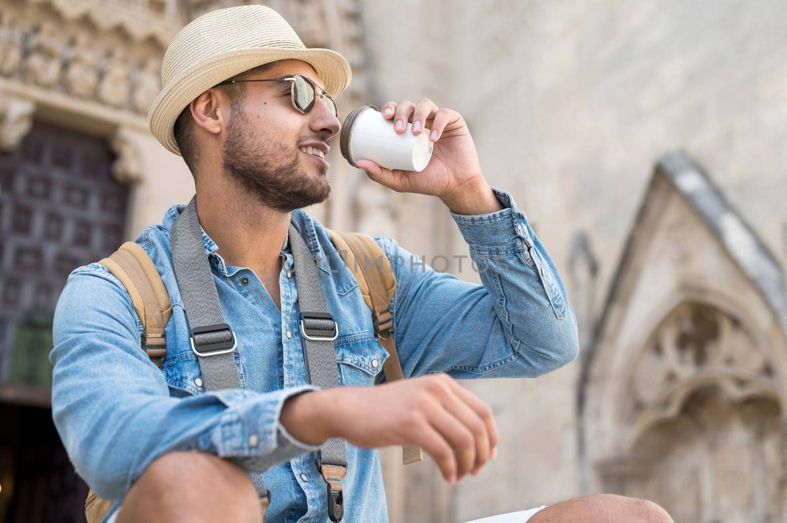 Happy young tourist man with coffee to go and backpack resting on street. High quality photo