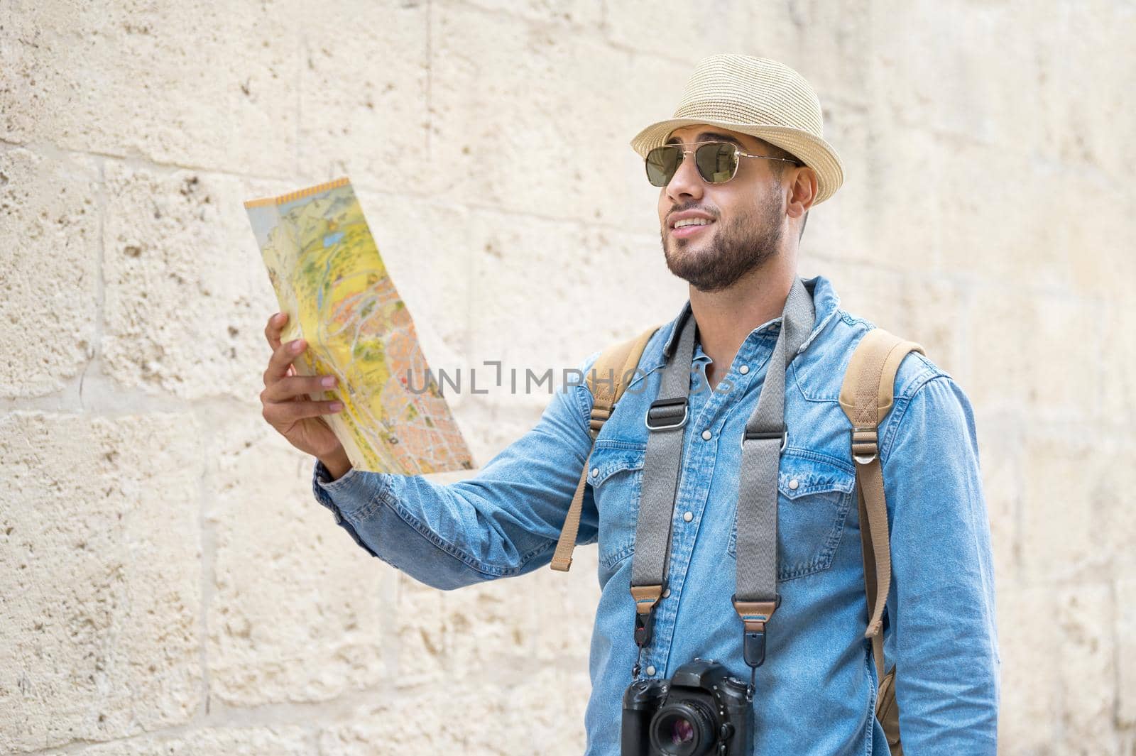 Young handsome man with tourist map looking around the city street. by HERRAEZ