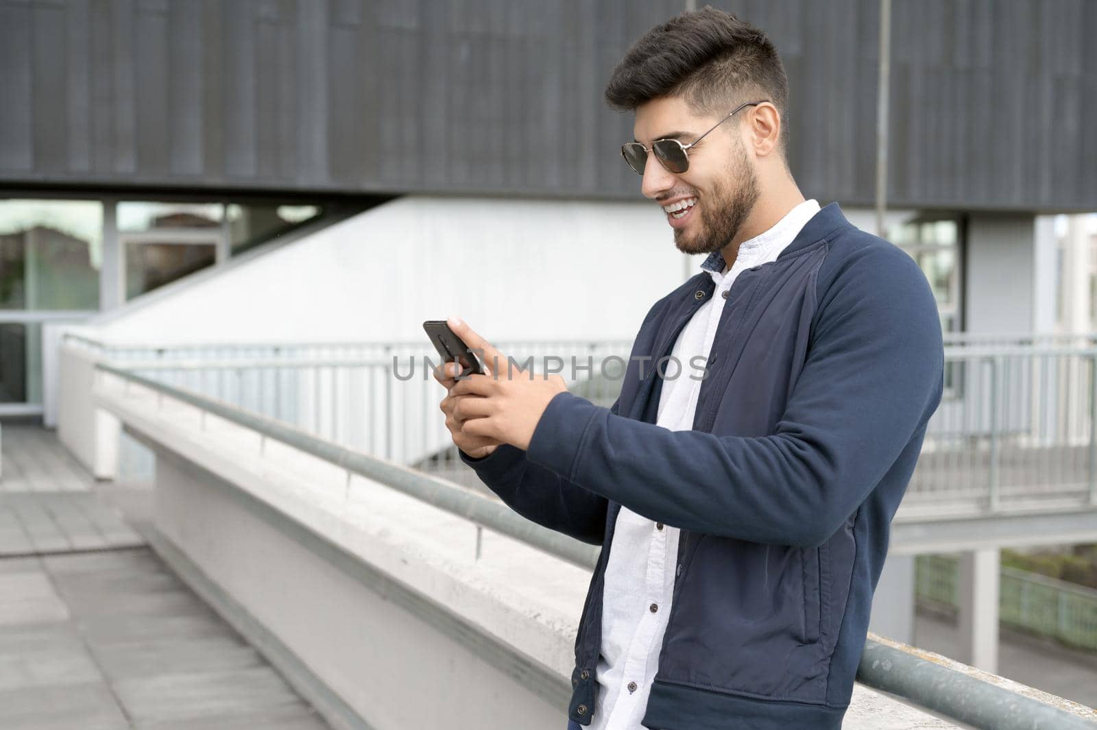 Handsome man using mobile phone app texting outside of office in urban city with skyscrapers buildings in the background. Young man holding smartphone for business work. High quality photo