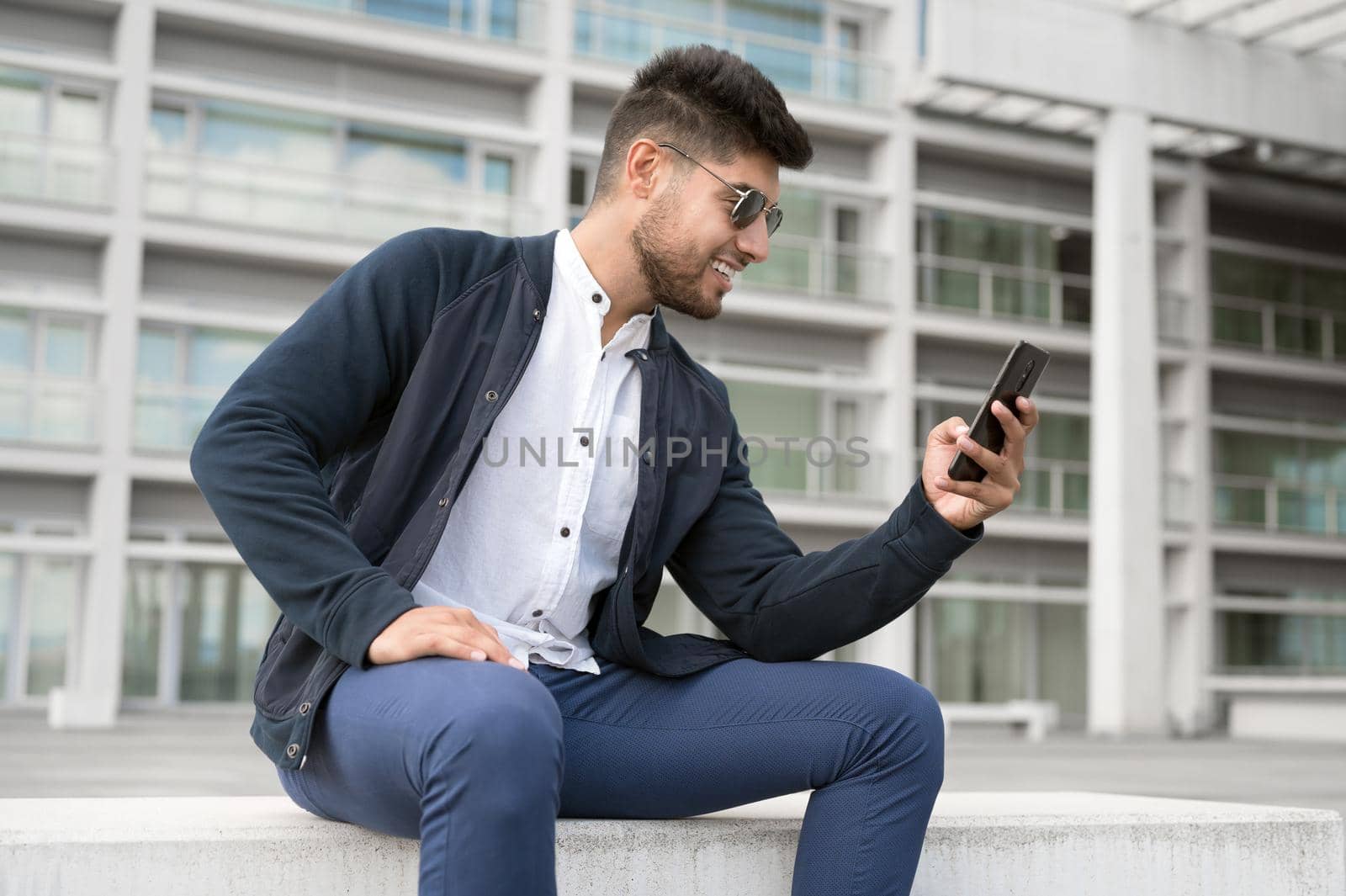 Young handsome men using smartphone in a city. Smiling young man texting on his mobile phone. Coffee break. Modern lifestyle, connection, business concept. by HERRAEZ