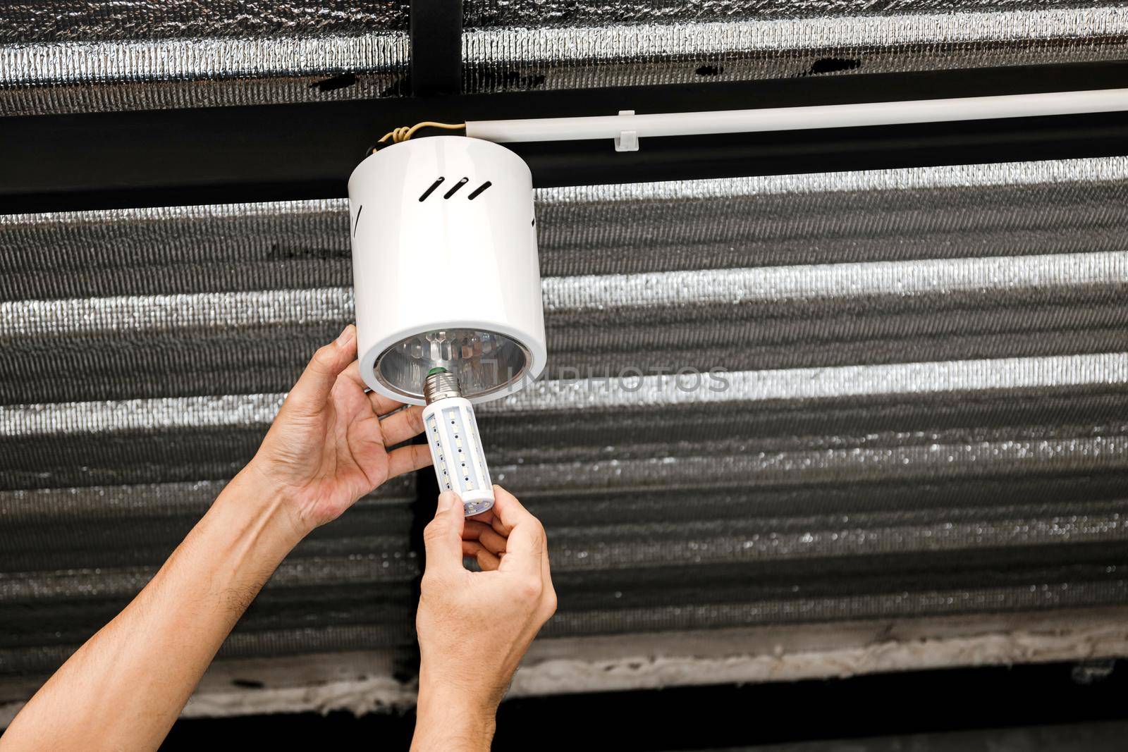 Human hand is installing an LED light bulb in a circular ceiling lamp. by wattanaphob