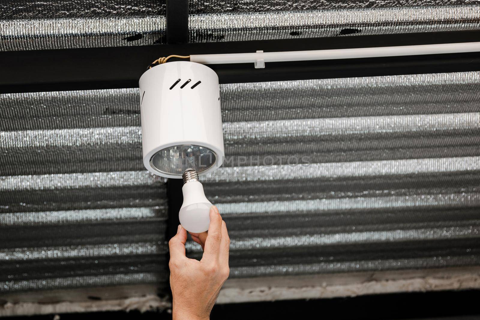 Close up human hand is installing an LED light bulb in a circular ceiling lamp.