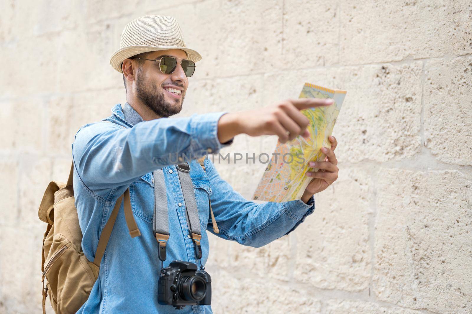 Handsome tourist man look at map while pointing finger in the direction of destination. Travel concept. Trip, backpacker tourist. by HERRAEZ