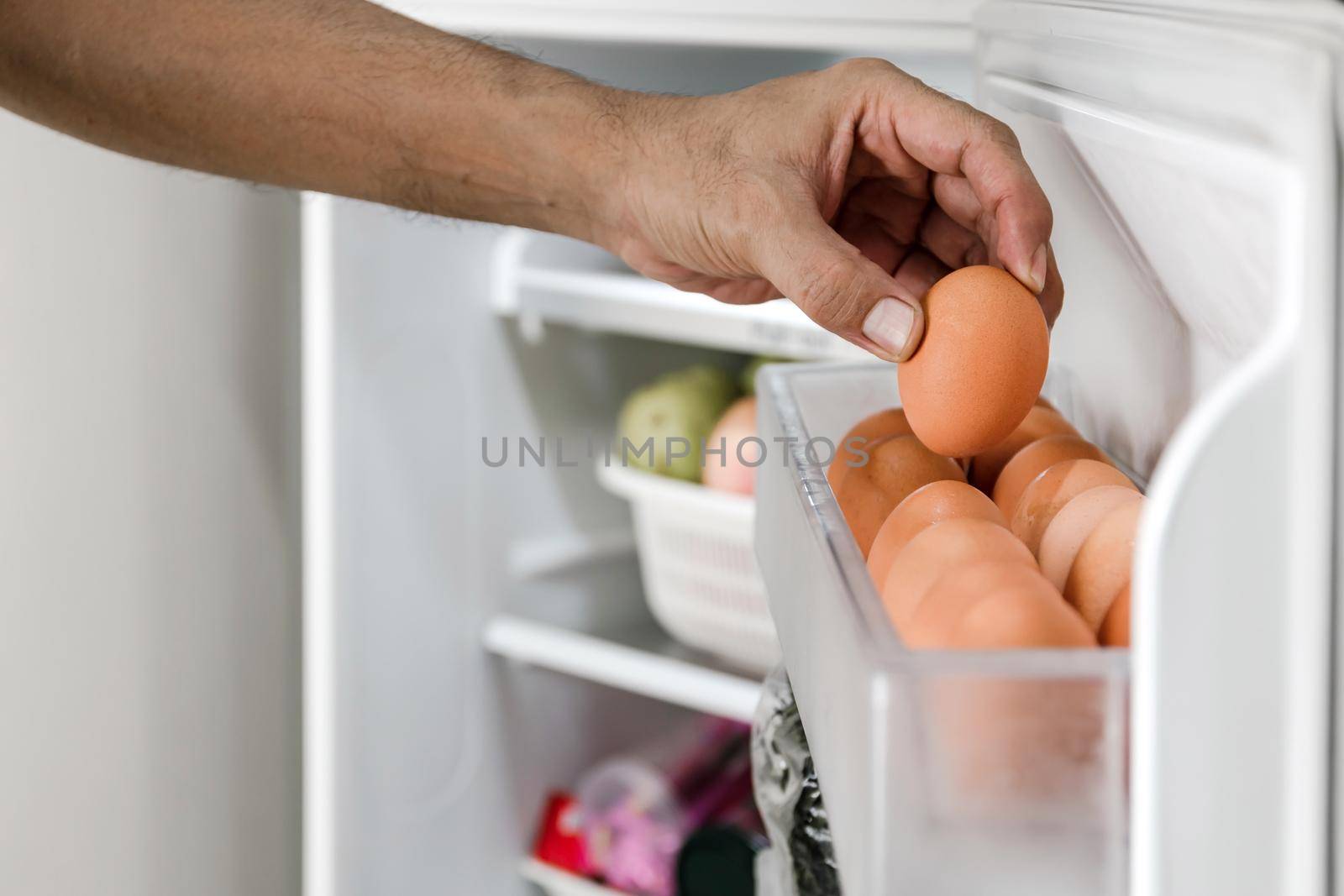 Close up human hands put chicken eggs in the egg-laying compartment in the refrigerator.