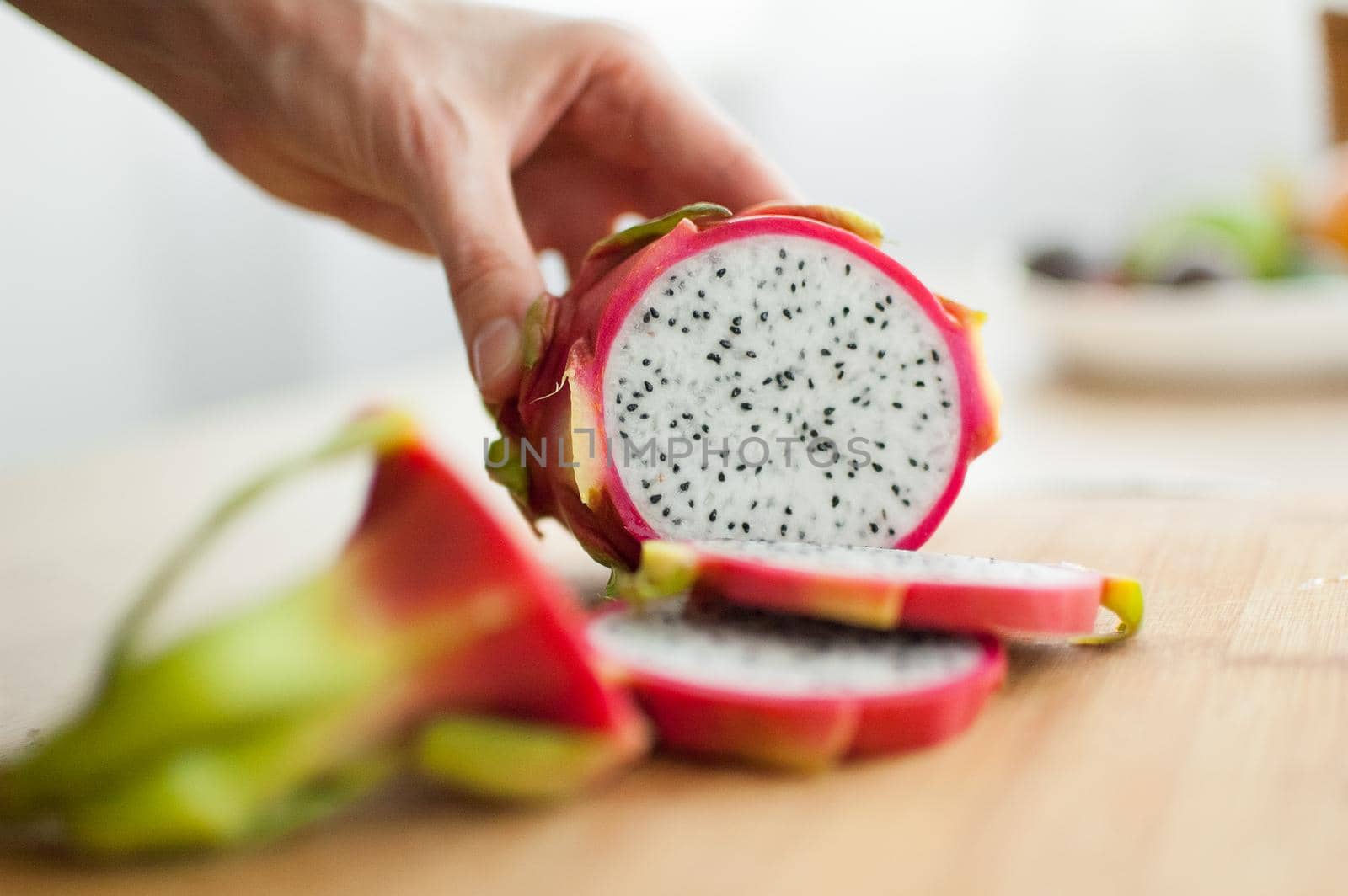 Female hands is cutting a dragon fruit or pitaya with pink skin and white pulp with black seeds on wooden cut board on the table. Exotic fruits, healthy eating concept.