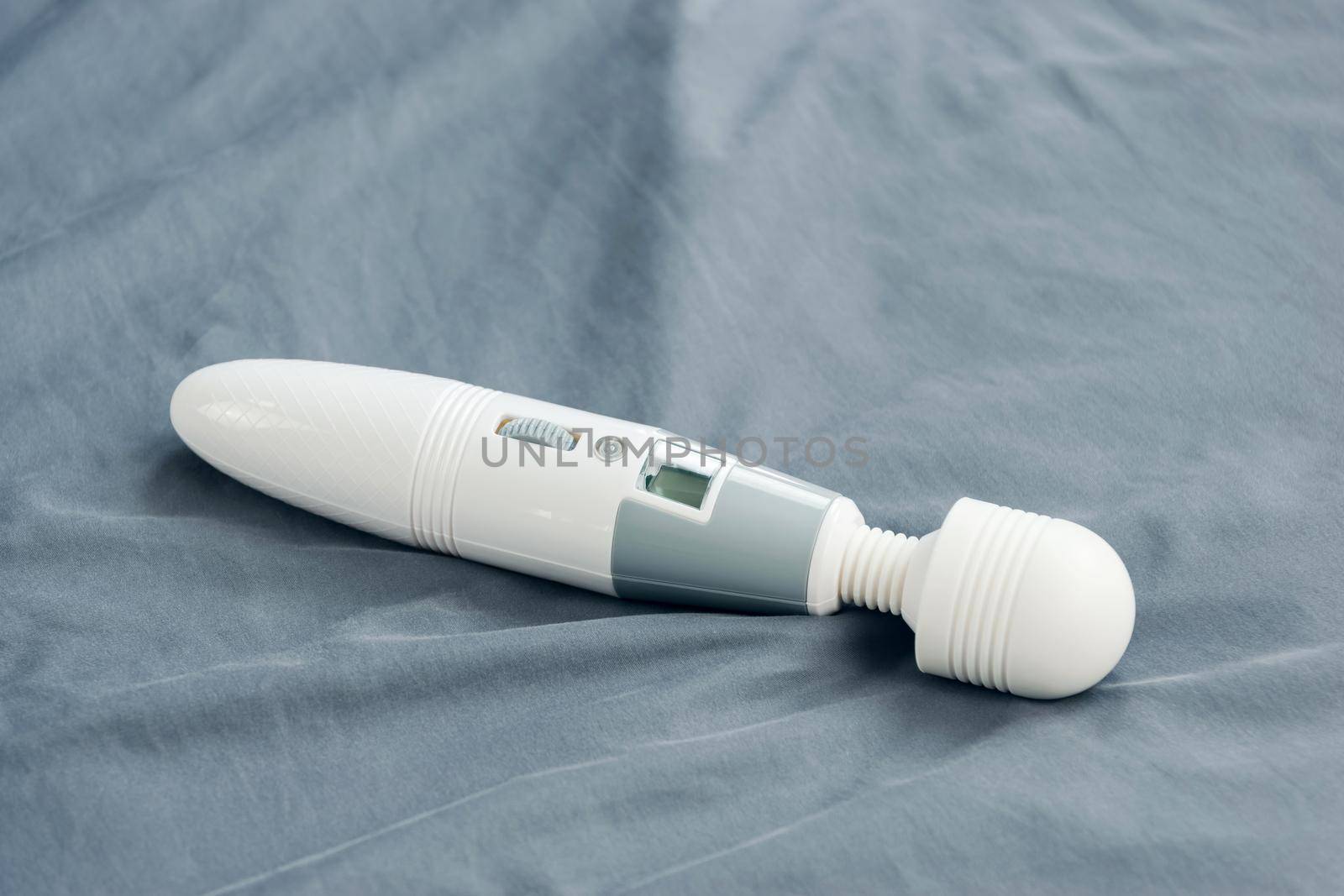 Close-up of vibrating sex toy lying on crumpled mattress.