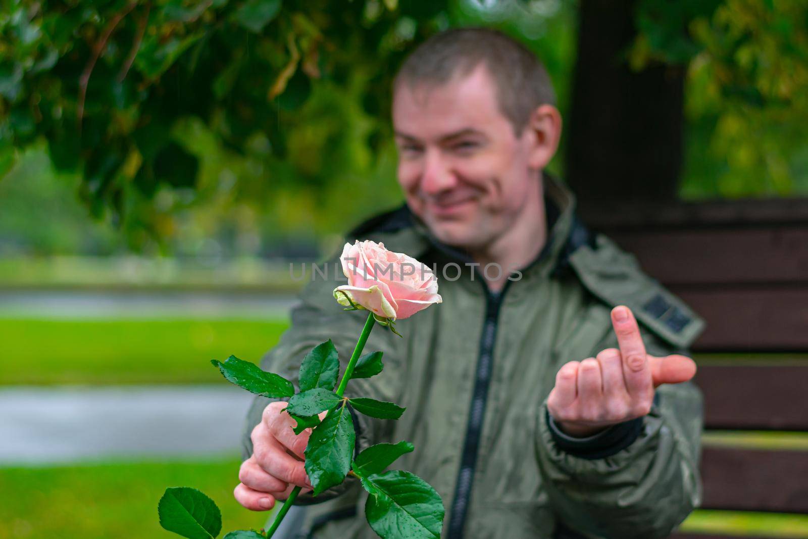 A rose in the hands of a smiling guy who beckons someone to him in rainy weather
