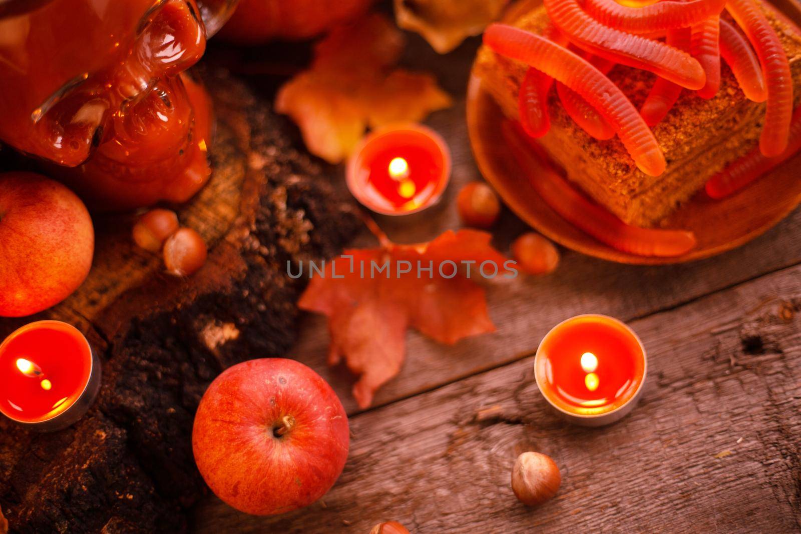Halloween food still life abstract background with pumpkins, apples, cake, gummy worms, skull red drink and candles