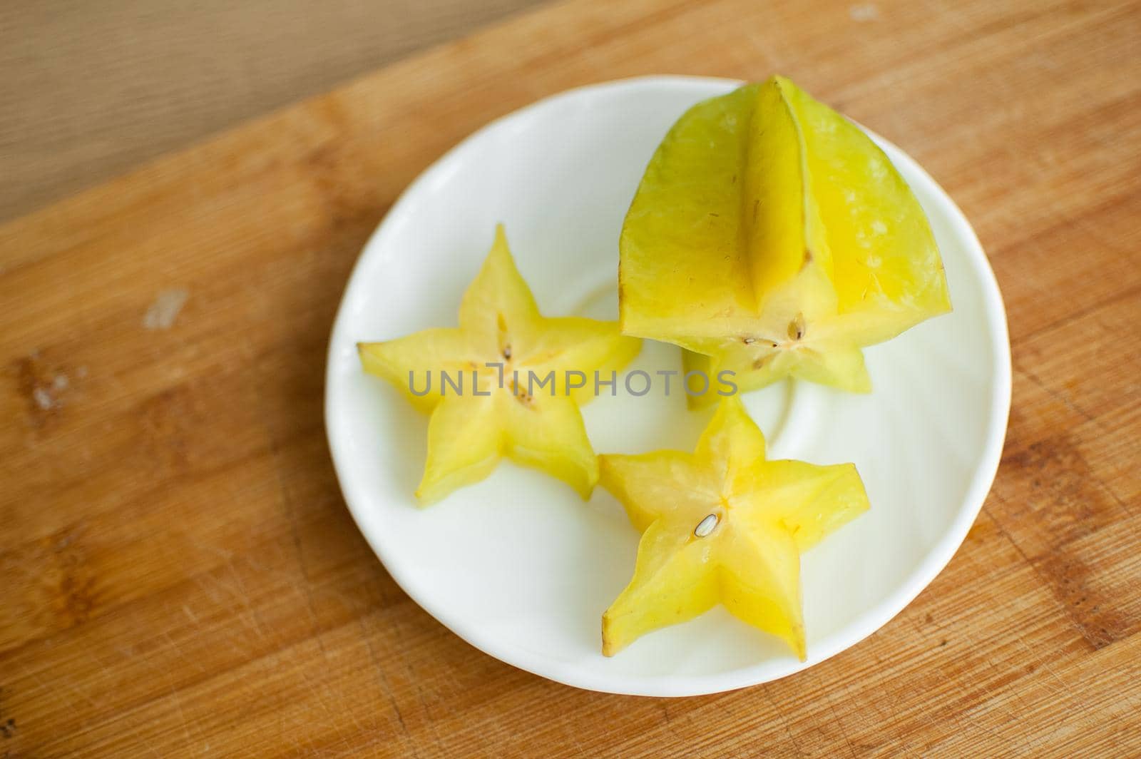 Exotic starfruit or averrhoa carambola on white plate on wooden cut board. Healthy food, fresh organic star apple fruit