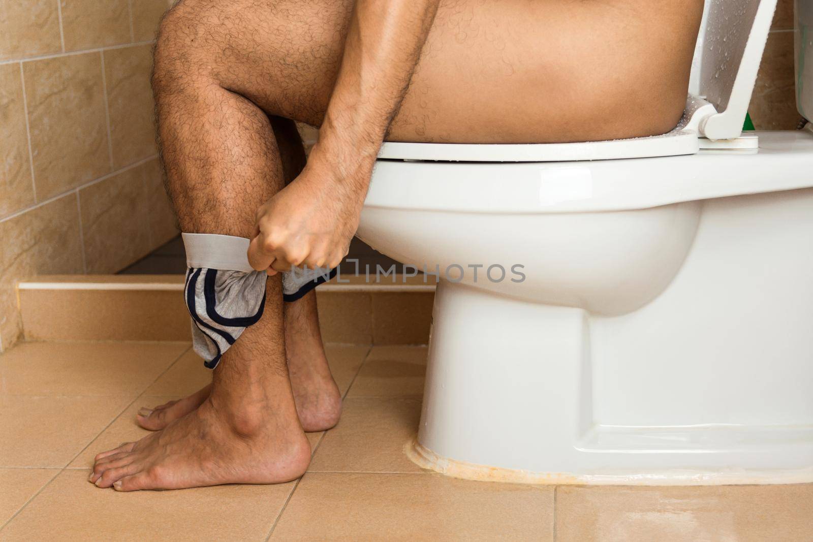 Close-up of a man's legs sitting stool on the toilet bowl.