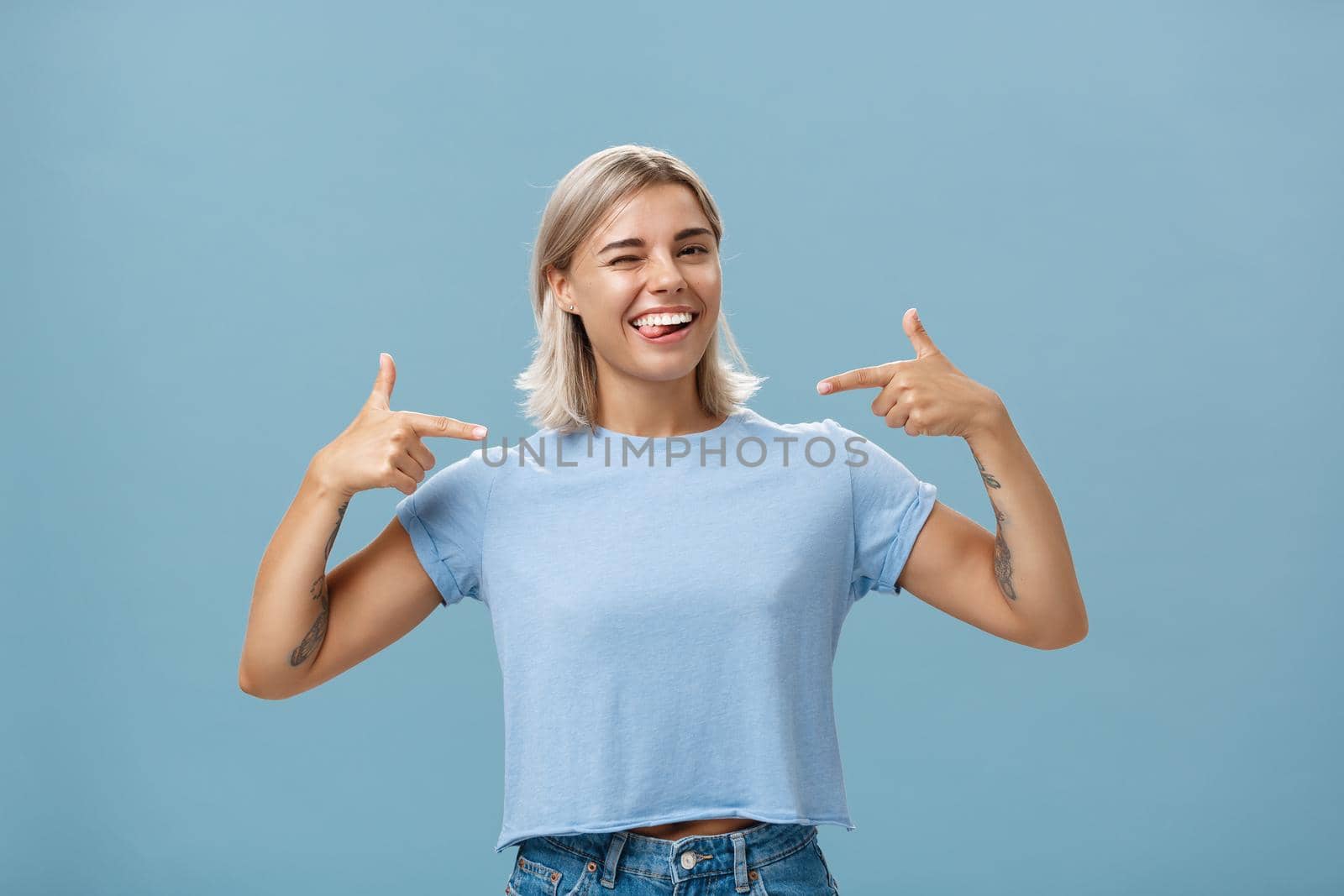 Girl proudly indicates at herself bragging with own achievements. Ambitious creative and smart attractive woman with tanned skin smiling joyfully sticking out tongue and winking pointing at chest.