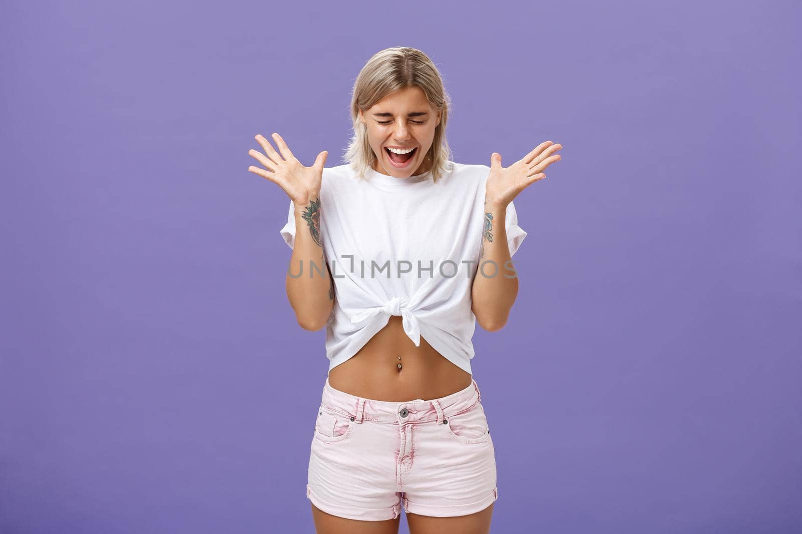 Studio shot of woman having mental breakdown screaming out loud shaking raised palms closing eyes and bending head down feeling scared and yelling from fear over purple background. Emotions concept