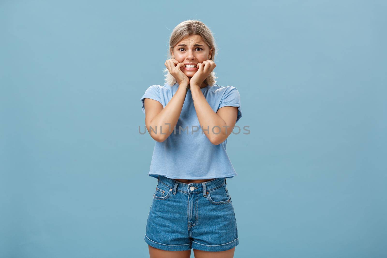 Attractive adult girl scared dad knows her secret standing over blue background frowning biting fingernails worrying and feeling anxious thinking about bad consequences insecure and nervous by Benzoix