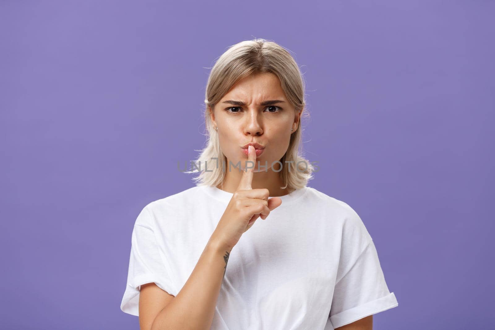 Lifestyle. Close-up shot of serious strict good-looking caucasian female with blond hair shushing at camera displeased and disappointed frowning holding index finger over folded lips in shush sign.