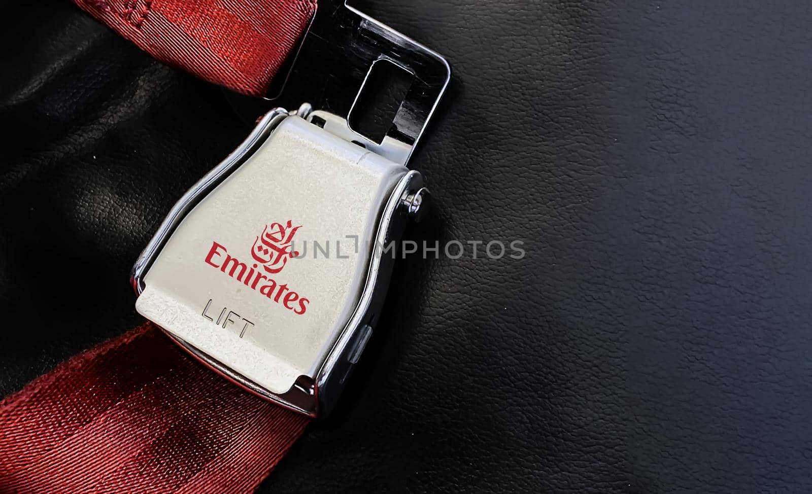 Dubai, UAE July 2021: Red lap belt of an empty seat inside an airplane with the Emirates logo printed on the metal.