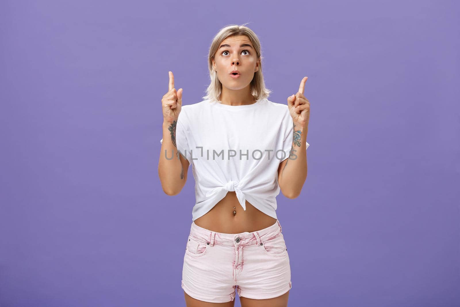 Girl dreaming become flight attendant being amazed with cool airplane flying in sky looking up with surprised impressed look saying wow pointing upwards posing over purple background by Benzoix