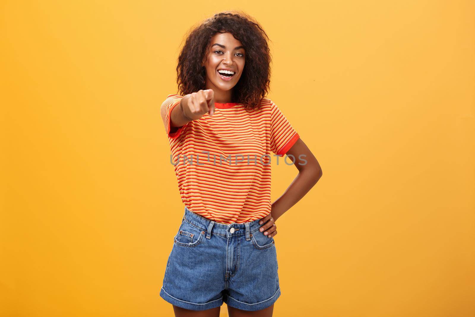 We hire you. Confident happy and awesome dark-skinned fashionable woman with curly hair holding hand on waist pointing at camera with index finger as if picking person or candidate, smiling. Body language concept