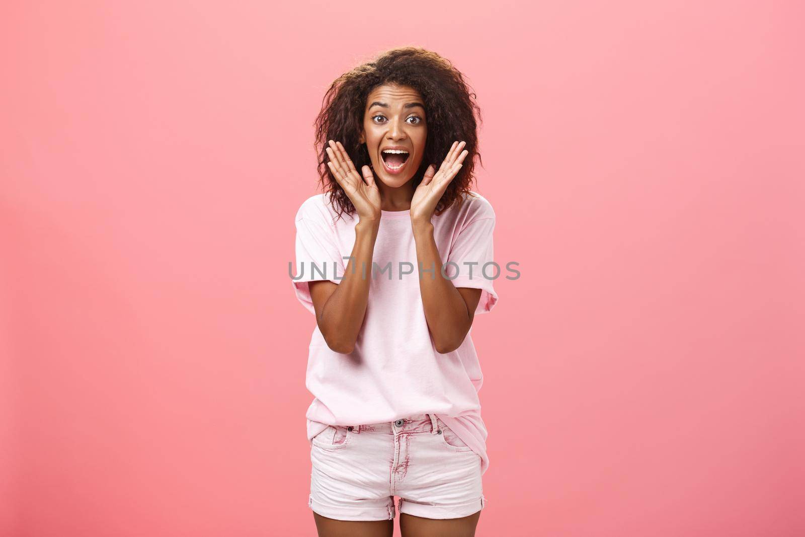 Indoor shot of expressive excited attractive dark-skinned adult woman in casual outfit yelling from amazement and joy holding palms near face reacting on awesome news with excitement and happiness. Lifestyle.