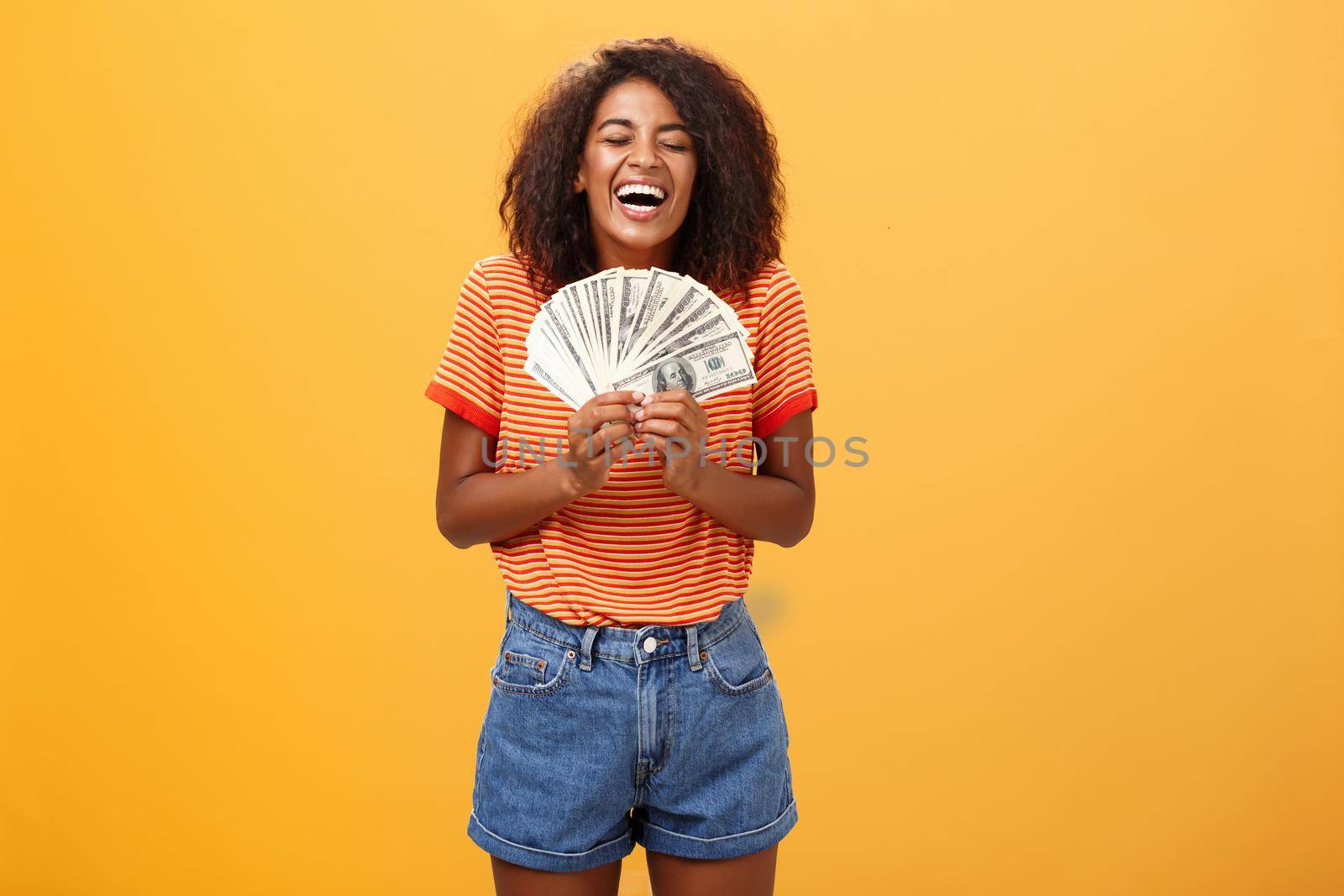 Finally girl rich. Portrait of happy charismatic stylish young female model receiving first payment holding lots of money and laughing from joy winning lottery ready waste cash over orange background by Benzoix