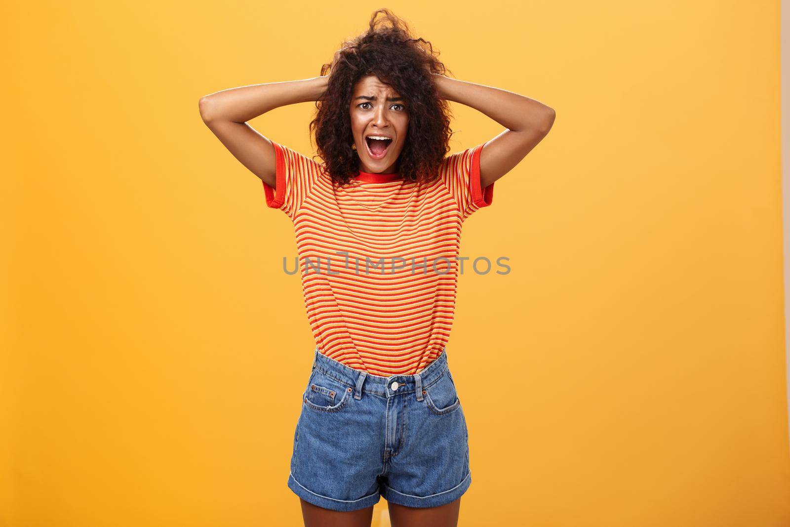 Girl panicking not being ready meet boyfriend parents. Portrait of shocked troubled and concerned gloomy girlfriend with afro hairstyle holding hands on hair yelling from shock over orange background by Benzoix