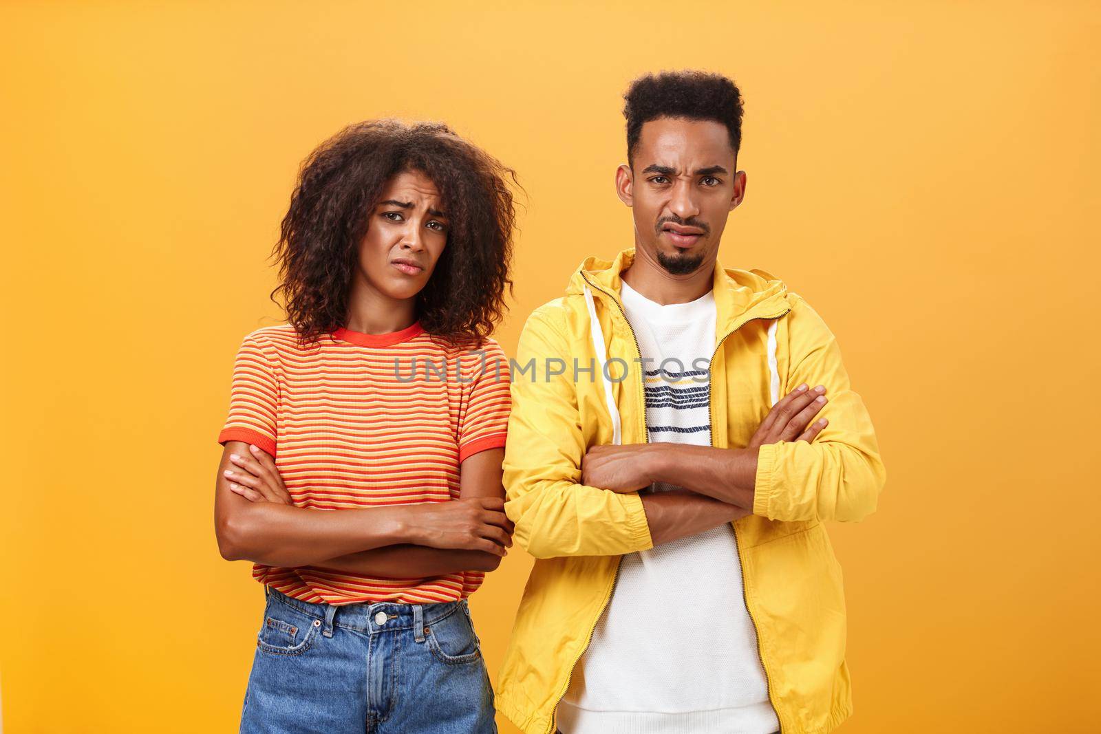 Two friends dislike lame idea of mate. Portrait of dissatisfied unimpressed african american man and woman crossing arms on chest in aversion frowning doubtful and disappointed over orange wall.