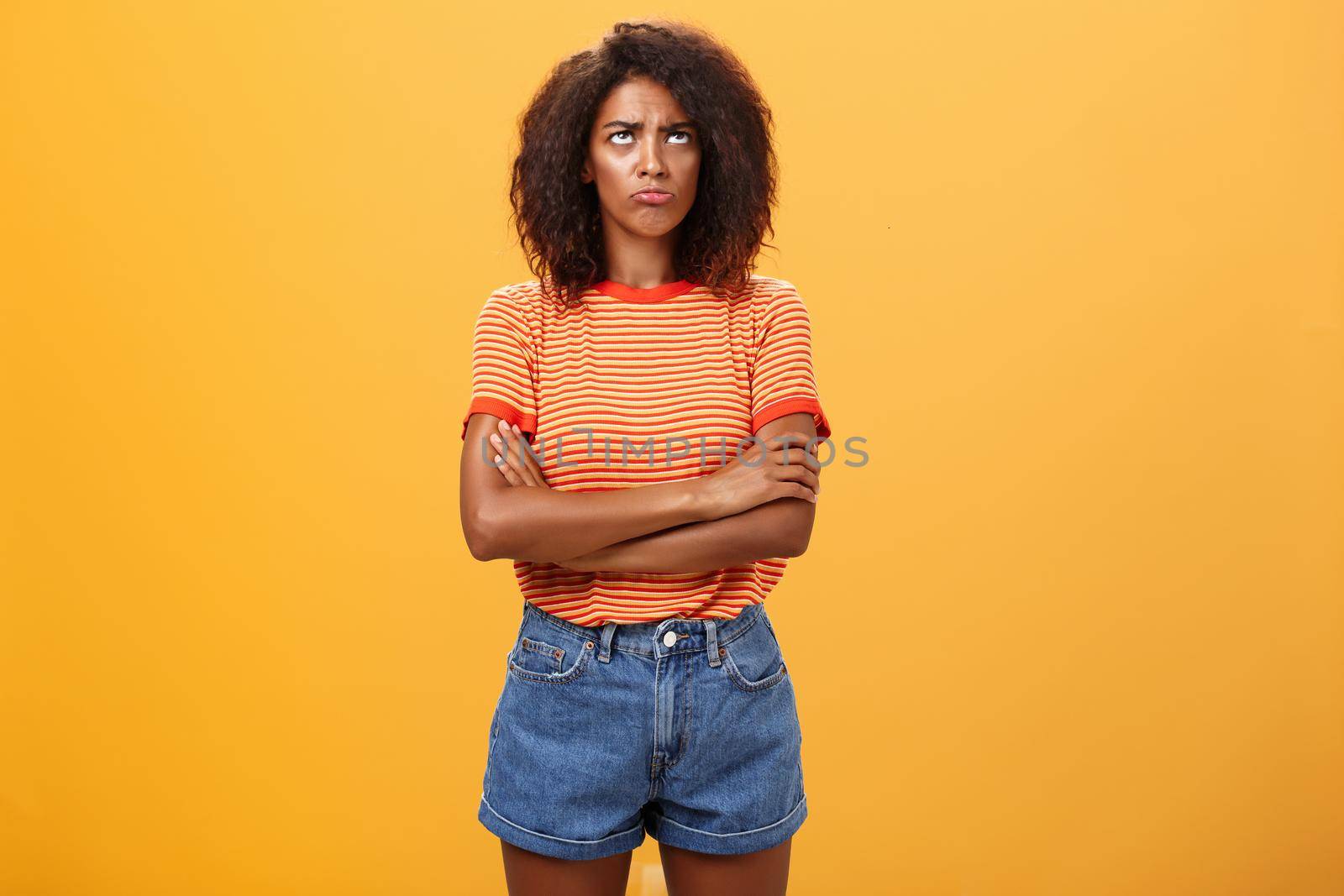 Why life so unfair. Portrait of cute offended and gloomy displeased african american young woman with afro hairstyle sulking pouting crossing arms on chest looking up with envy or jealousy by Benzoix
