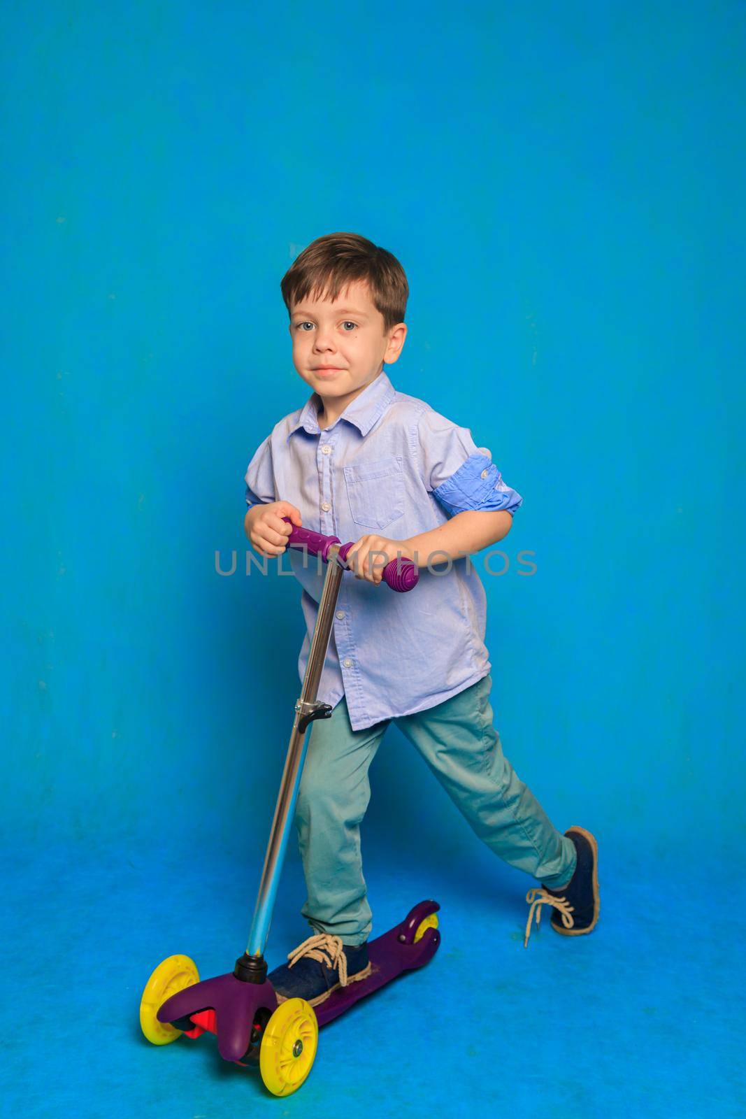 A boy on a scooter on a blue background . An article about children's scooters. An article about the choice of a scooter for a child. A happy child. Blue background and a boy. Copy Space