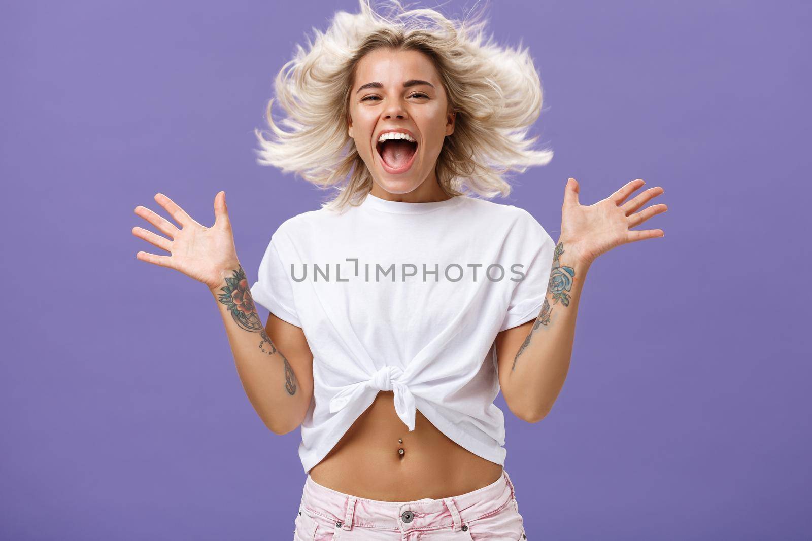 Lifestyle. Studio shot of happy carefree and pleased joyful woman with blonde hair spreading palms aside in delighted pose smiling broadly and gazing entertained at camera jumping while having fun.