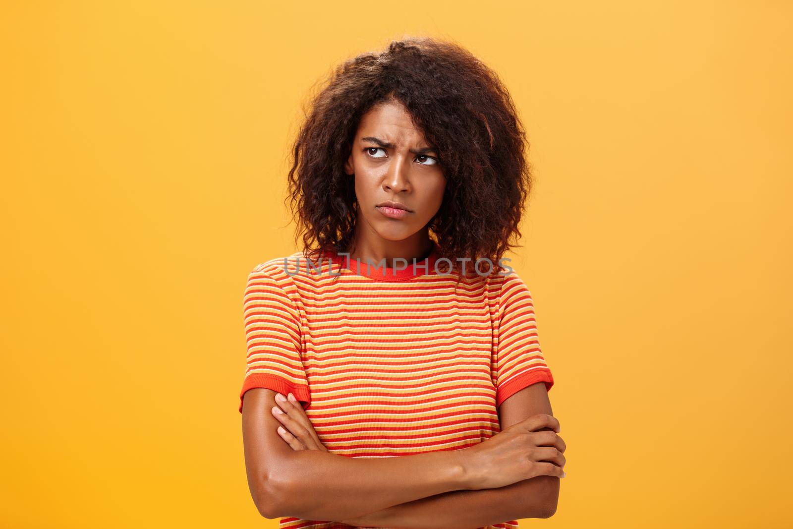 Why life so cruel and unfair. Gloomy displeased and sad cute african american young woman with curly hairstyle crossing arms on chest in offended pose frowning looking left jealous and unhappy.