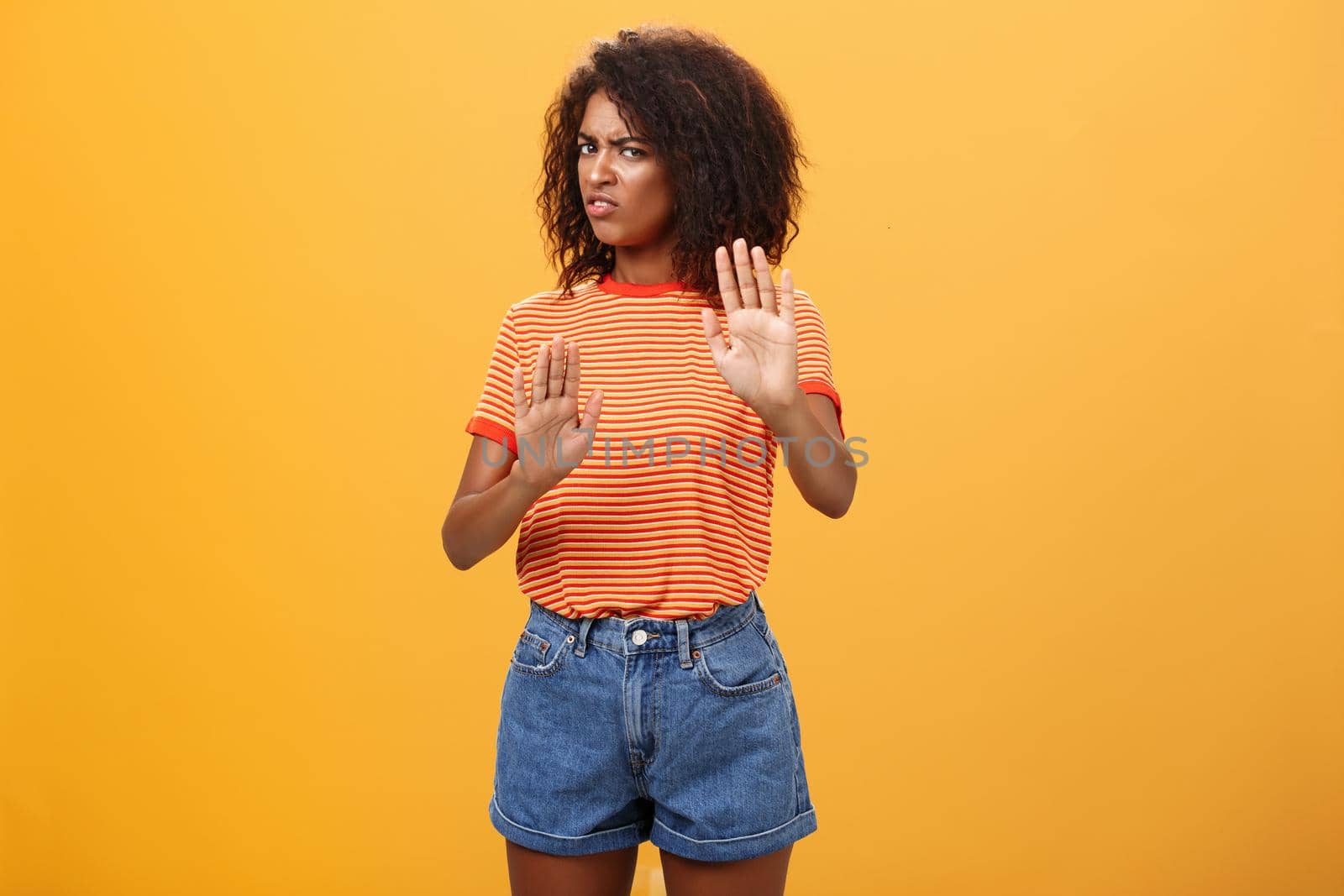 No I refuse. Intense suspicious and displeased smart african-american female rejecting bad offer pulling raised palms turning away with aversion and dissatisfied look against orange background.