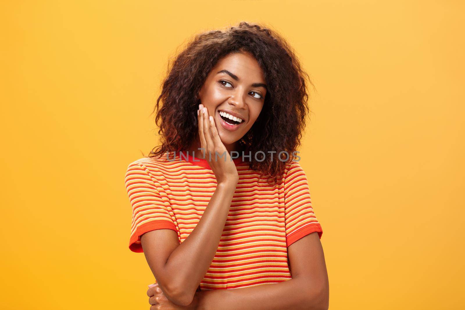 Cute creative and feminine stylish african american young female in striped t-shirt leaning head on palm gazing left with curious and adorable expression delightfully listening interesting story. Lifestyle.