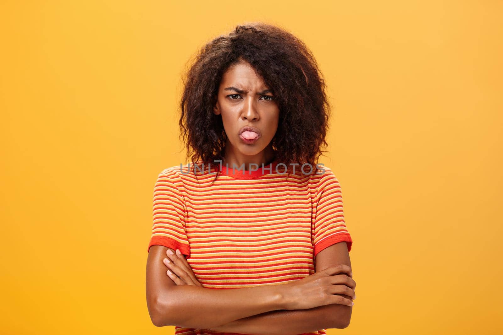 You offended me apologize. Displeased childish attractive adult woman in striped t-shirt holding hands crossed sticking out tongue and frowning having bad temper being dissatisfied and angry.