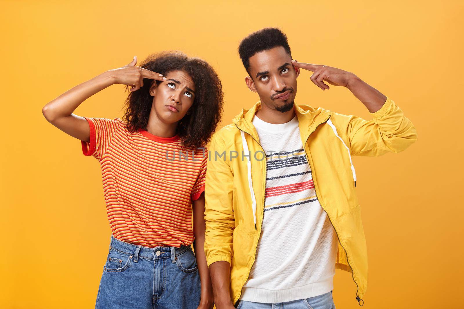 Pair of african american lovers getting annoyed with parents scolding, teaching them how live sexual life rolling eyes up from irritation holding finger gun near temples standing close to each other. Relationship concept