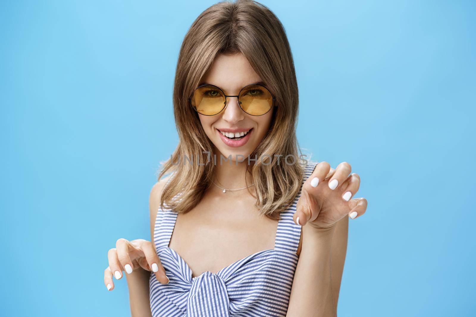 Sensual woman feeling like attractive wild cat raising hands like paws saying meow looking daring and flirty at camera, seducing with confident gaze, wearing stylish sunglasses and striped top. Body language concept