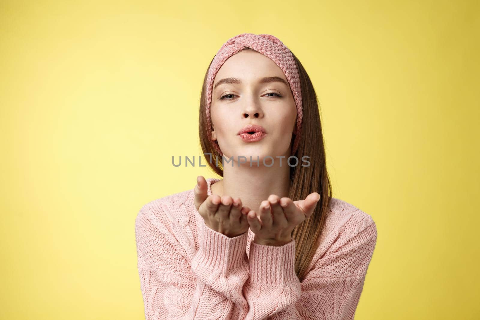 Happy valentines day. Charming romantic and sensual young flirty woman in knitted headband, sweater extending palms near folded lips sending air mwah, blowing kiss tender and gentle.