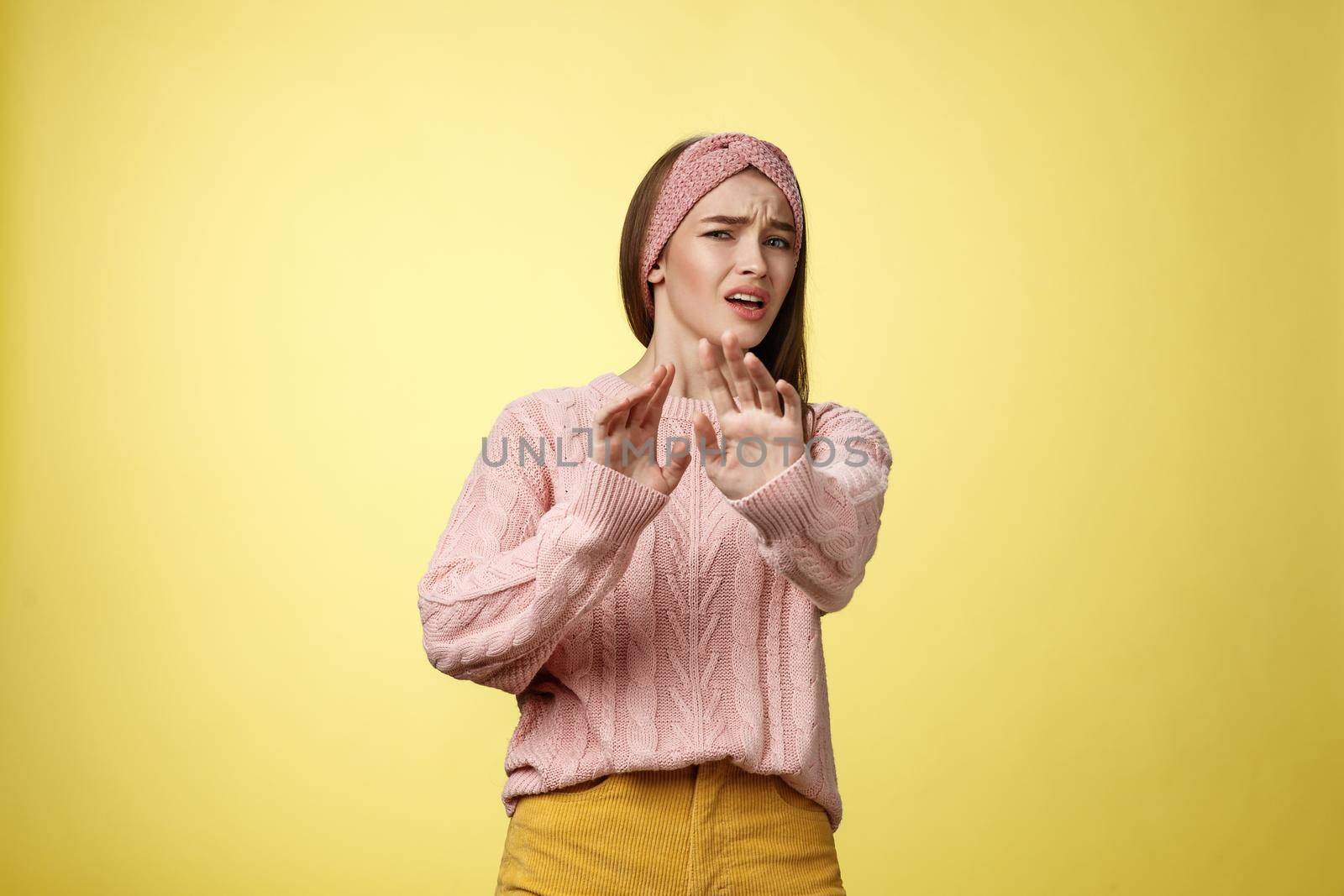 Omg no. Cute young european schoolgirl step back stooping grimacing disgusted and displeased turning away reluctant expressing aversion extending palm in rejection, refusal gesture over yellow wall.