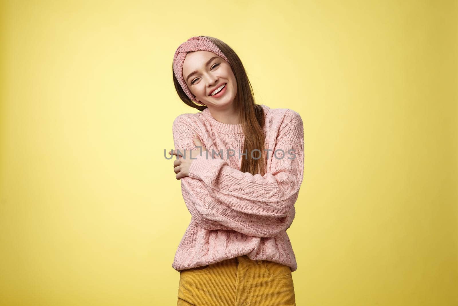 Cozy charming friendly young smiling girl in knitted warm comfortable sweater, grinning joyfully tilt head emracing herself, crossing arms, hugging feeling safe and happy, posing against yellow wall by Benzoix