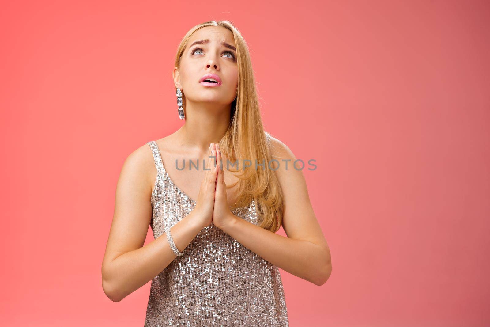 Hopeful worried concerned faithful blond woman in silver dress praying talking god wishing family okay press palms together supplicating nervously begging, standing red background stylish dress.