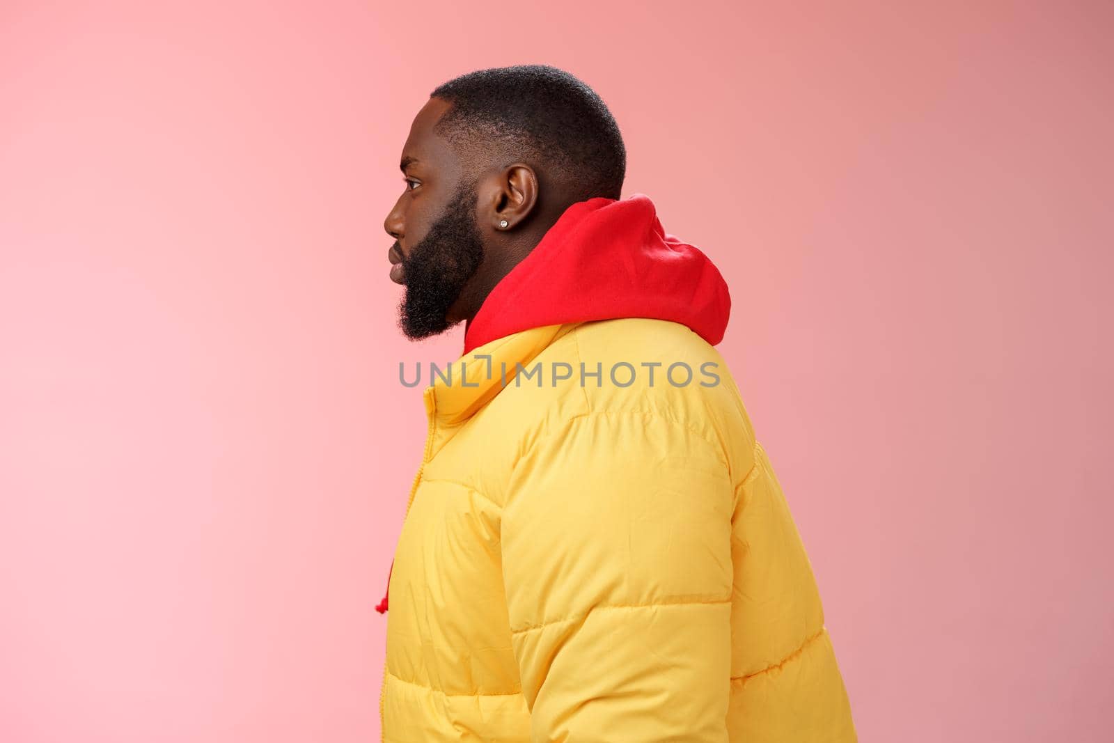 Profile studio shot bearded young 25s african guy in yellow jacket red hoodie look left normal unbothered relaxed expression standing queue order fastfood pink background, waiting take-away by Benzoix