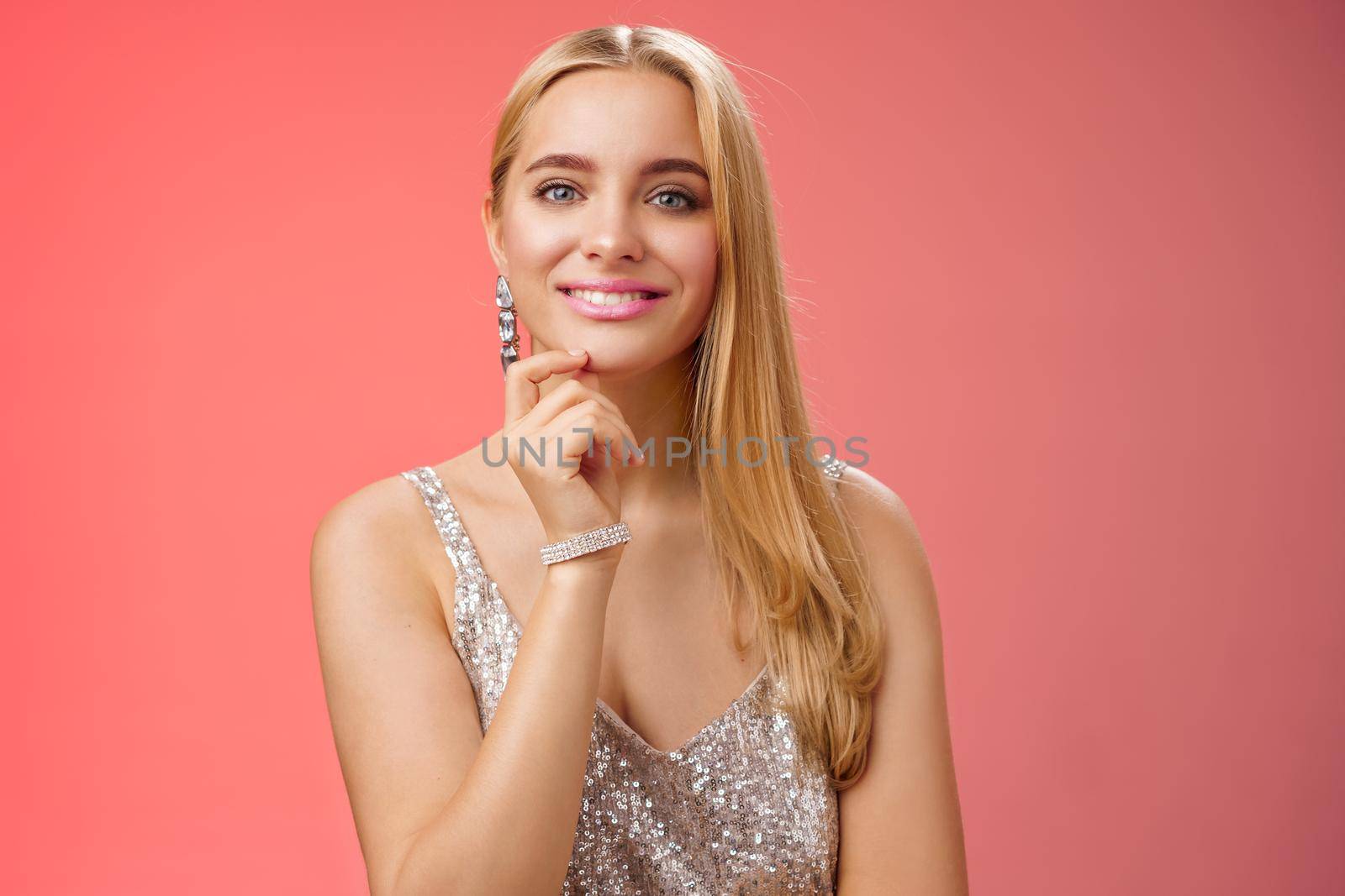 Waist-up shot elegant good-looking wealthy young blond woman in brilliant accessorize silver glittering stylish dress touch chin have clever interesting idea smiling curiously, red background by Benzoix