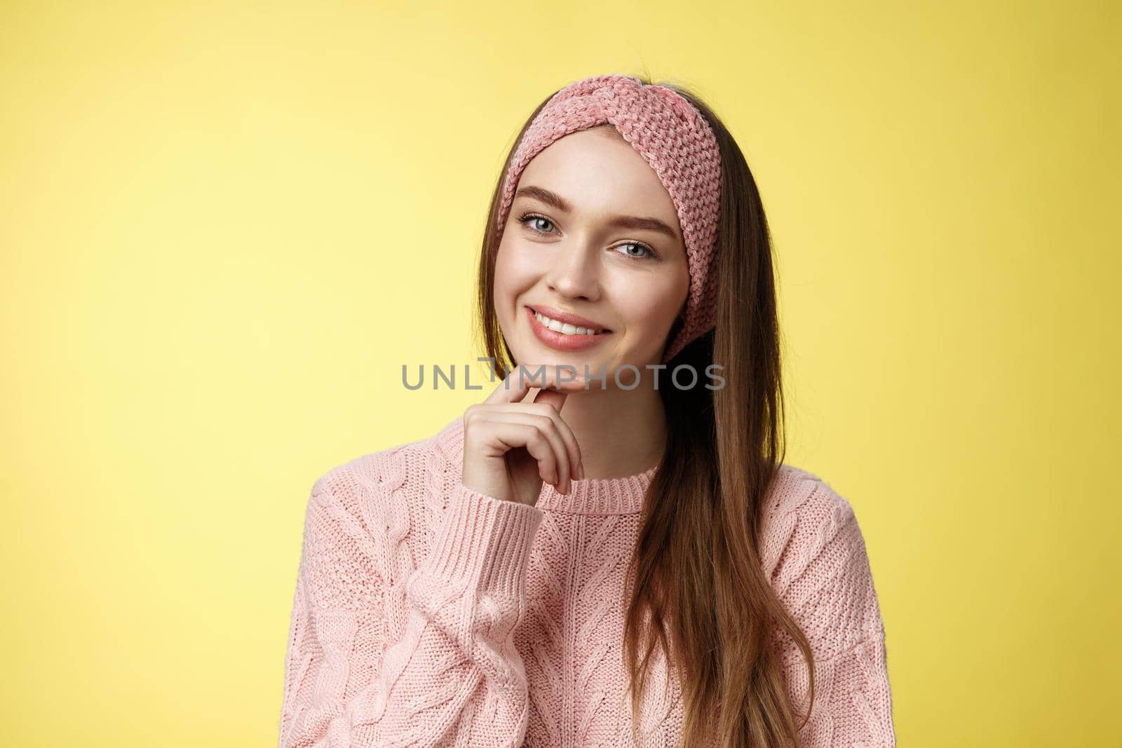 Happy young european woman in knitted headband, sweater tilting head touching chin and smiling silly, taking care of skin, feeling face glittering looking clear and healthy after skincare treatment by Benzoix